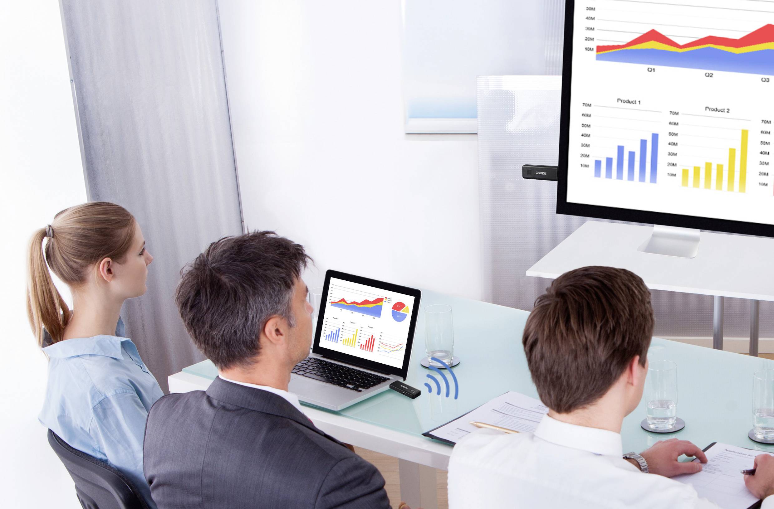 Trois personnes sont assises à une table et regardent les diagrammes d'une présentation. Sur un écran, on peut voir des graphiques à barres et des graphiques linéaires.