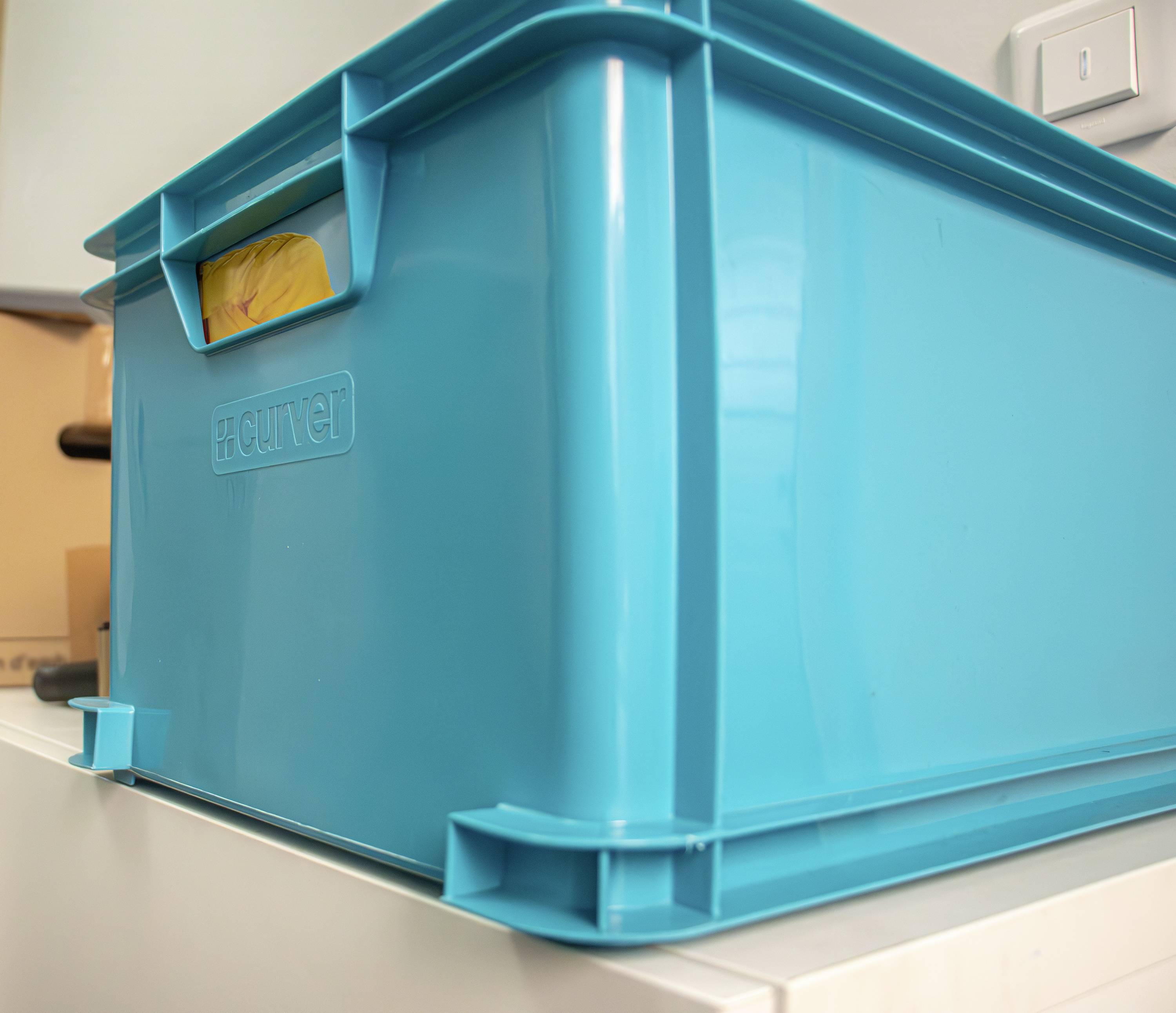 Un grand récipient en plastique turquoise est posé sur une table. Le récipient possède une poignée sur le côté et porte le logo 'Curver'.