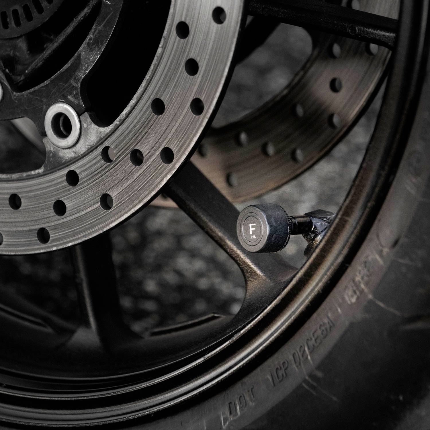 Gros plan d'un disque de frein de vélo avec un motif de perforations et une valve de pneu noire à proximité.