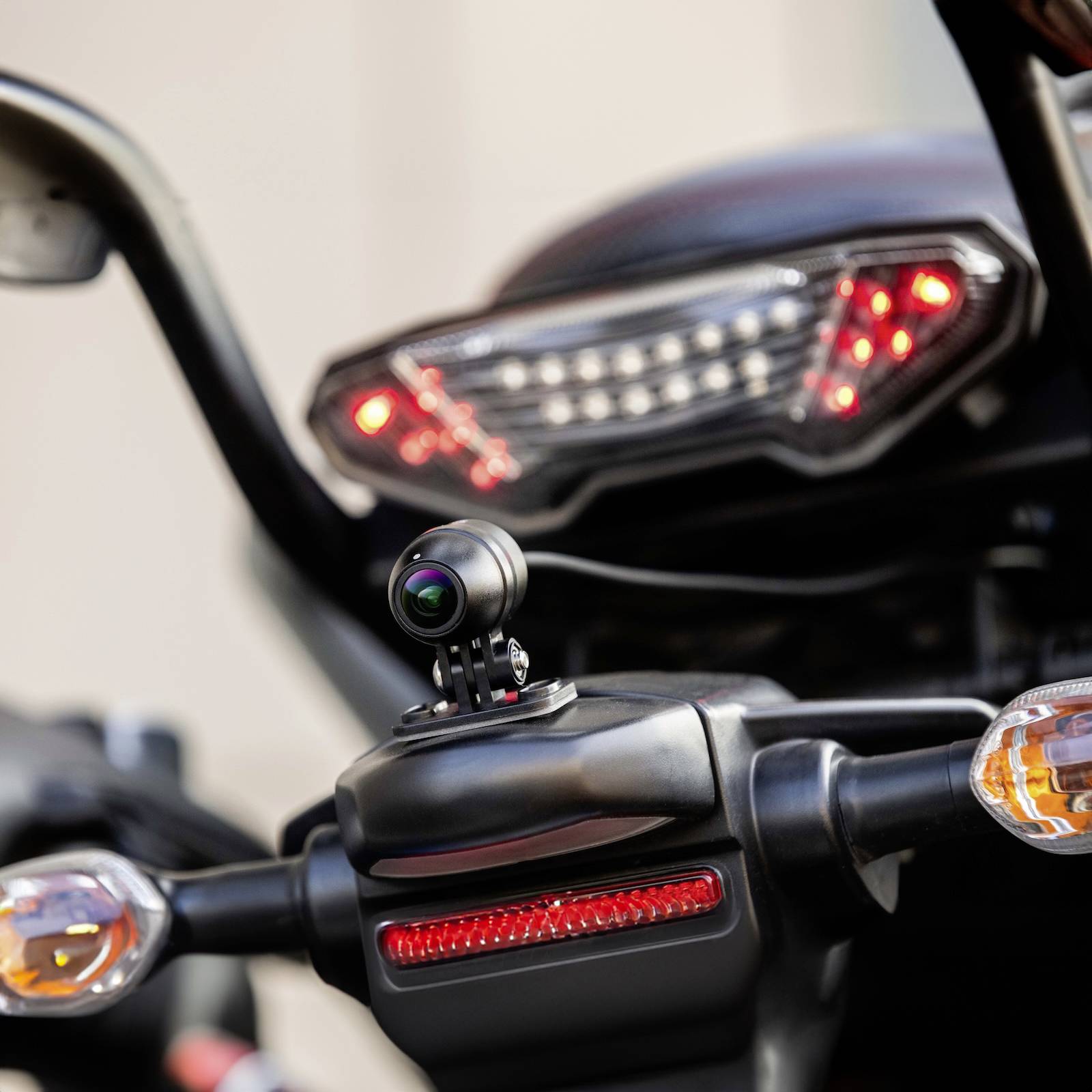 Une caméra de recul est montée sur un guidon de moto pour surveiller la zone arrière. Des feux de freinage sont visibles en arrière-plan.