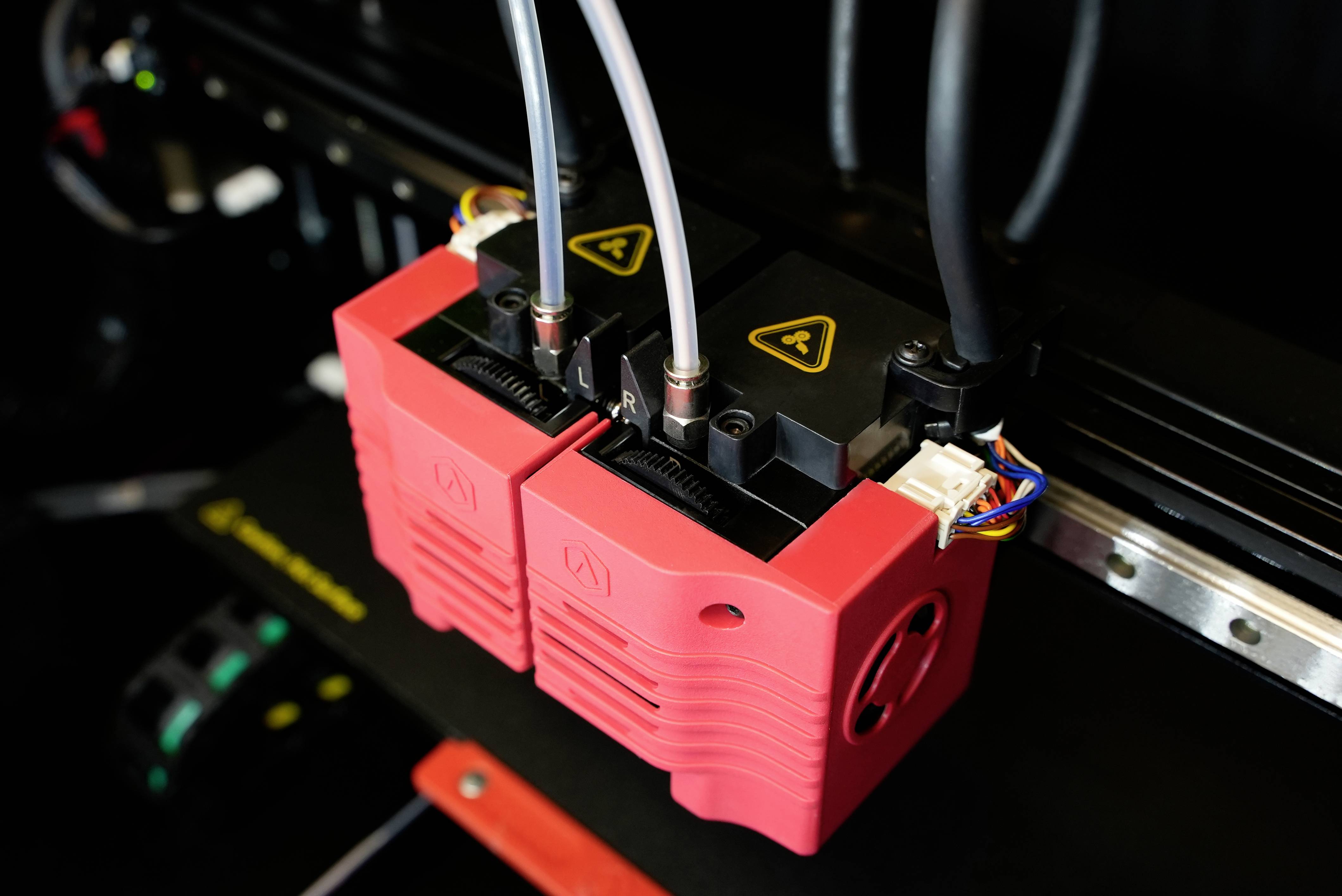 Buses d'imprimantes 3D avec des capuchons rouges et des tuyaux noirs connectés à un plateau d'impression, au premier plan.