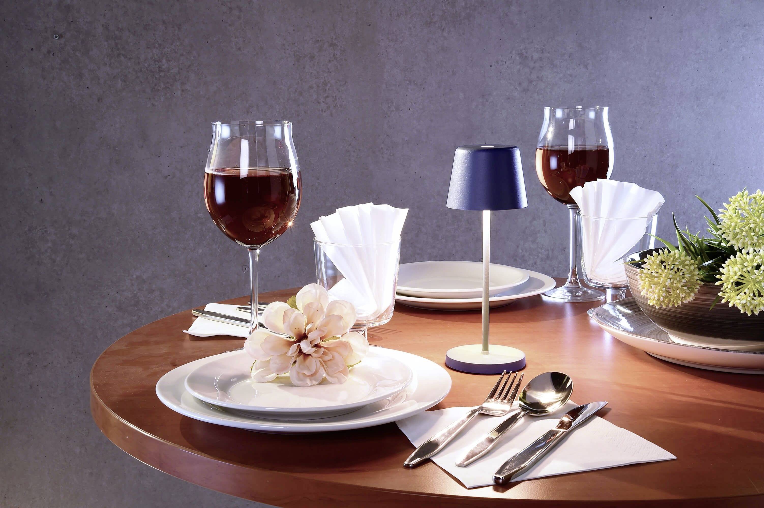 Une table élégamment dressée avec des verres à vin, des couverts, des serviettes et un arrangement floral sur une table en bois, sous un éclairage doux.