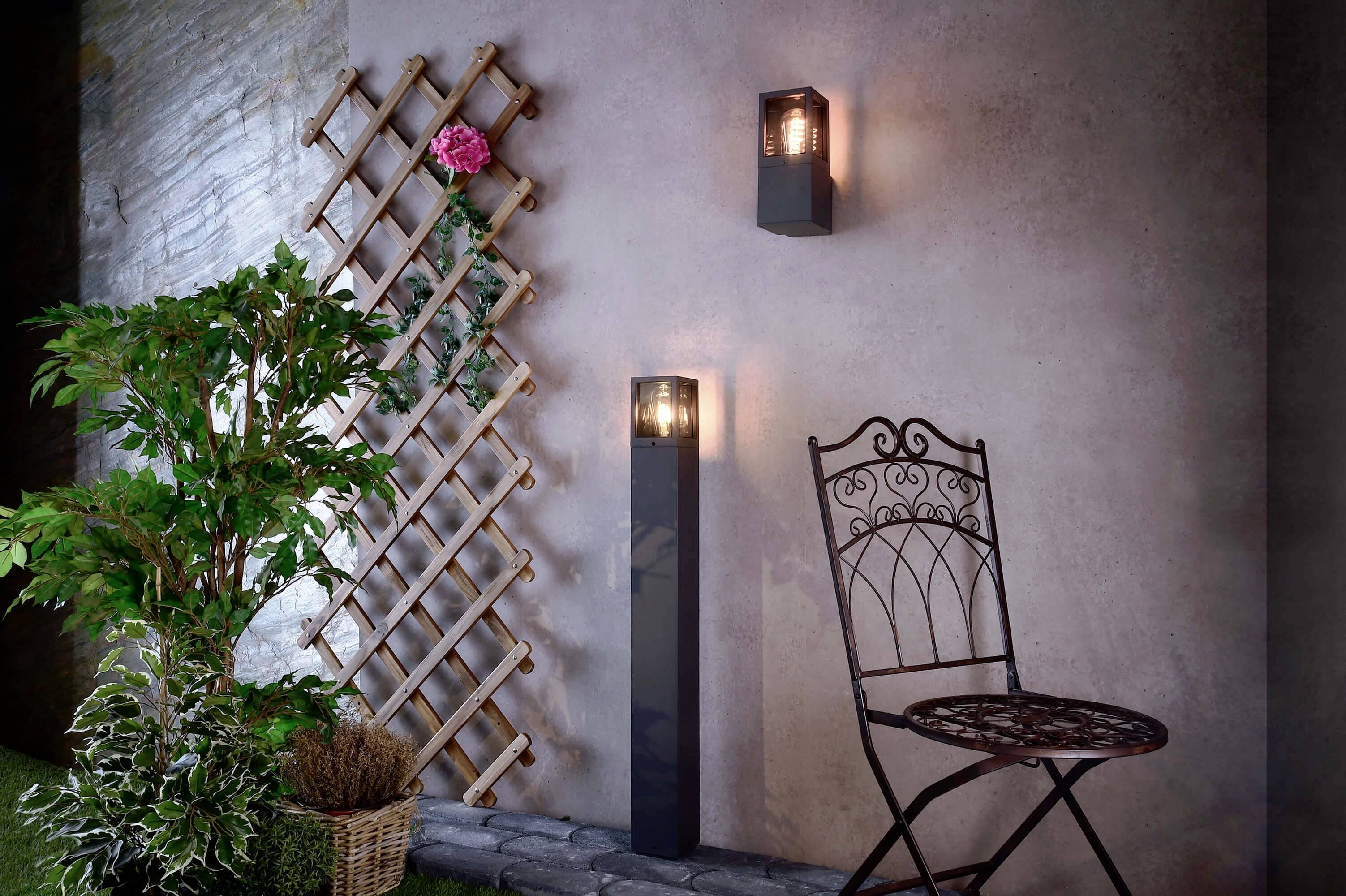 Coin d'un jardin avec une chaise en métal, un rosier grimpant, un luminaire mural haut et bas, éclairé ; ambiance décorative.
