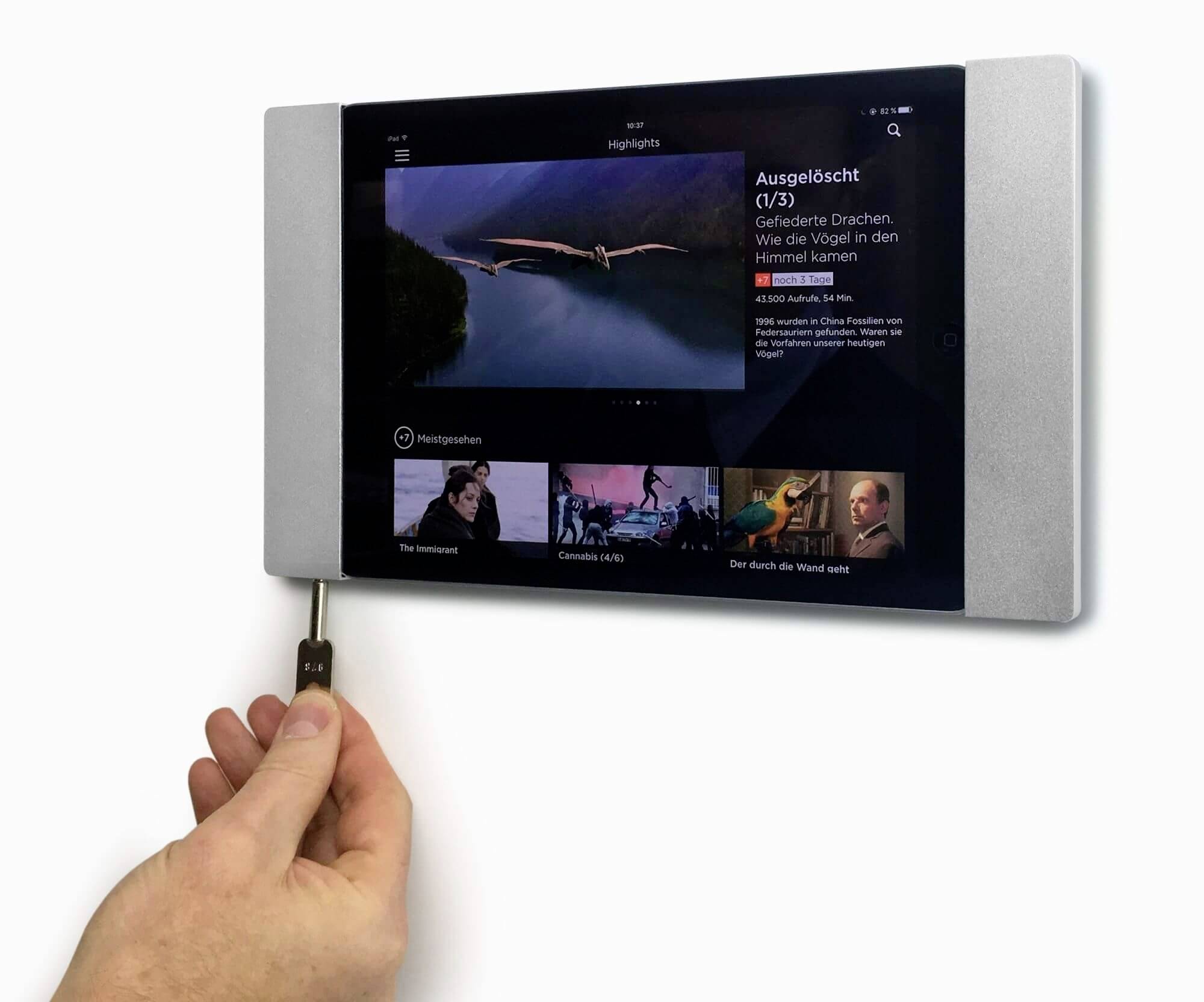 Une personne tient un stylet sur une tablette montée au mur. L'écran affiche des films à sélectionner.