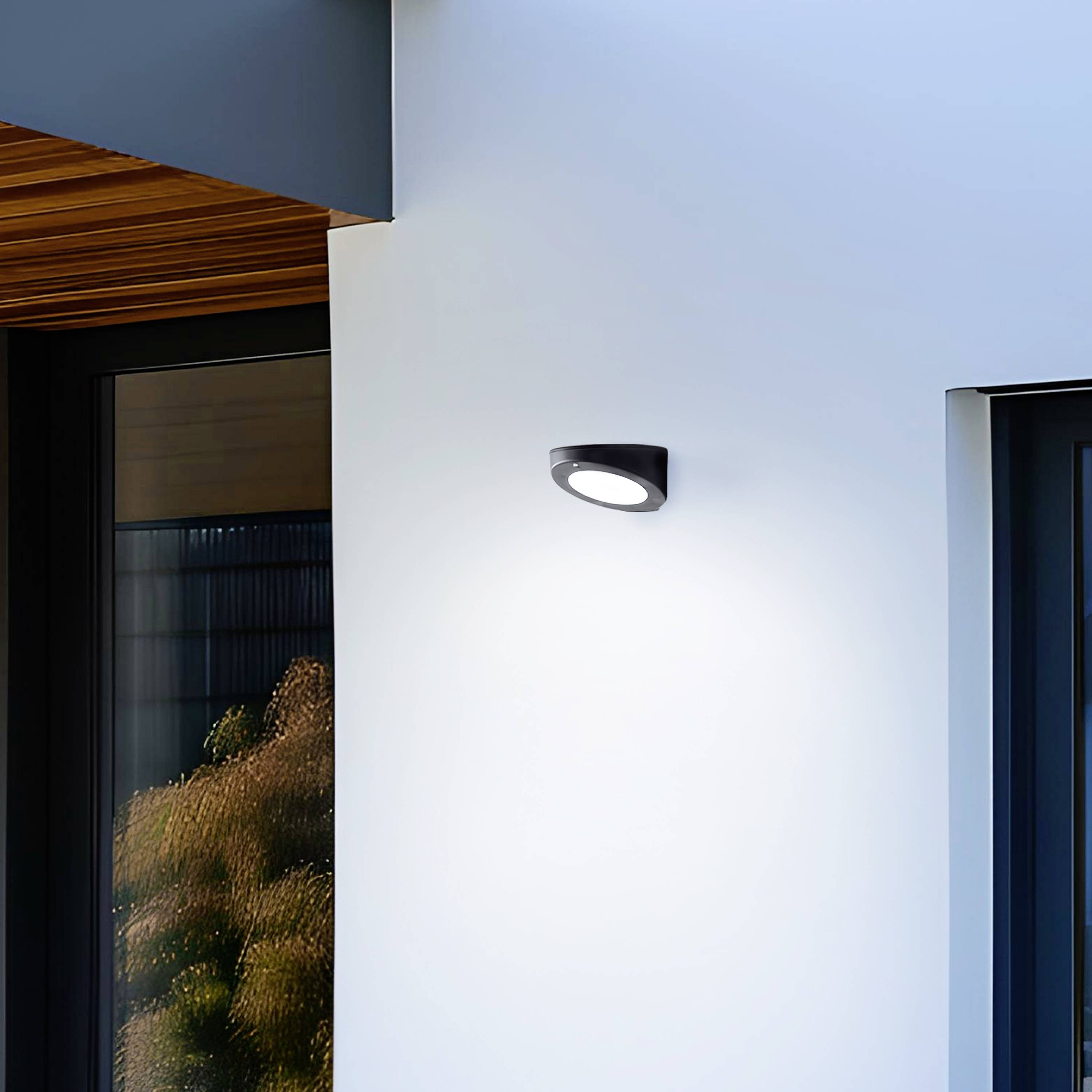 Vue extérieure d'une maison moderne avec un mur blanc et un luminaire extérieur noir à côté d'un cadre de fenêtre gris.