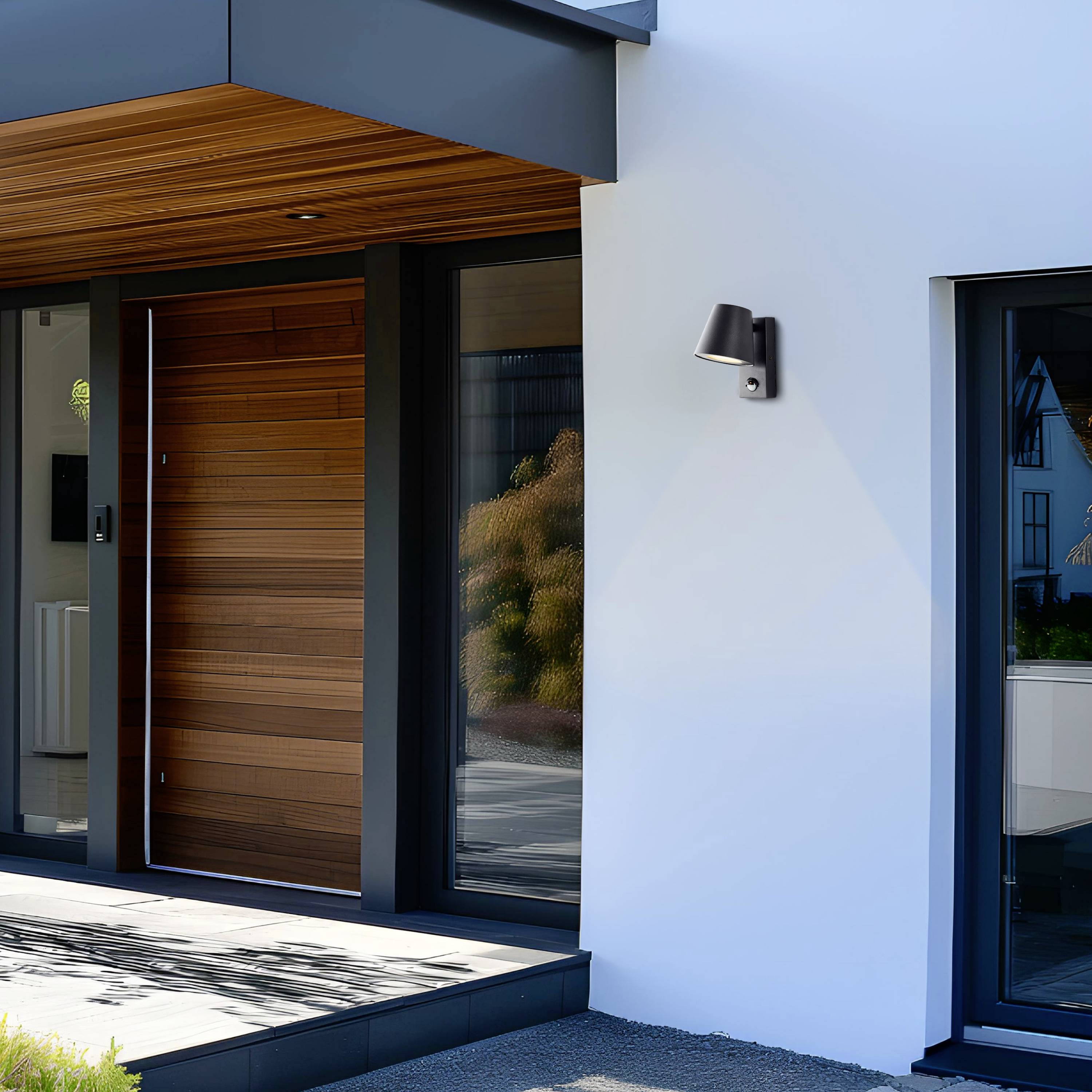 Façade moderne de maison avec revêtement en bois et accents métalliques, lampes à côté de la porte d'entrée, reflets d'arbres dans les fenêtres.