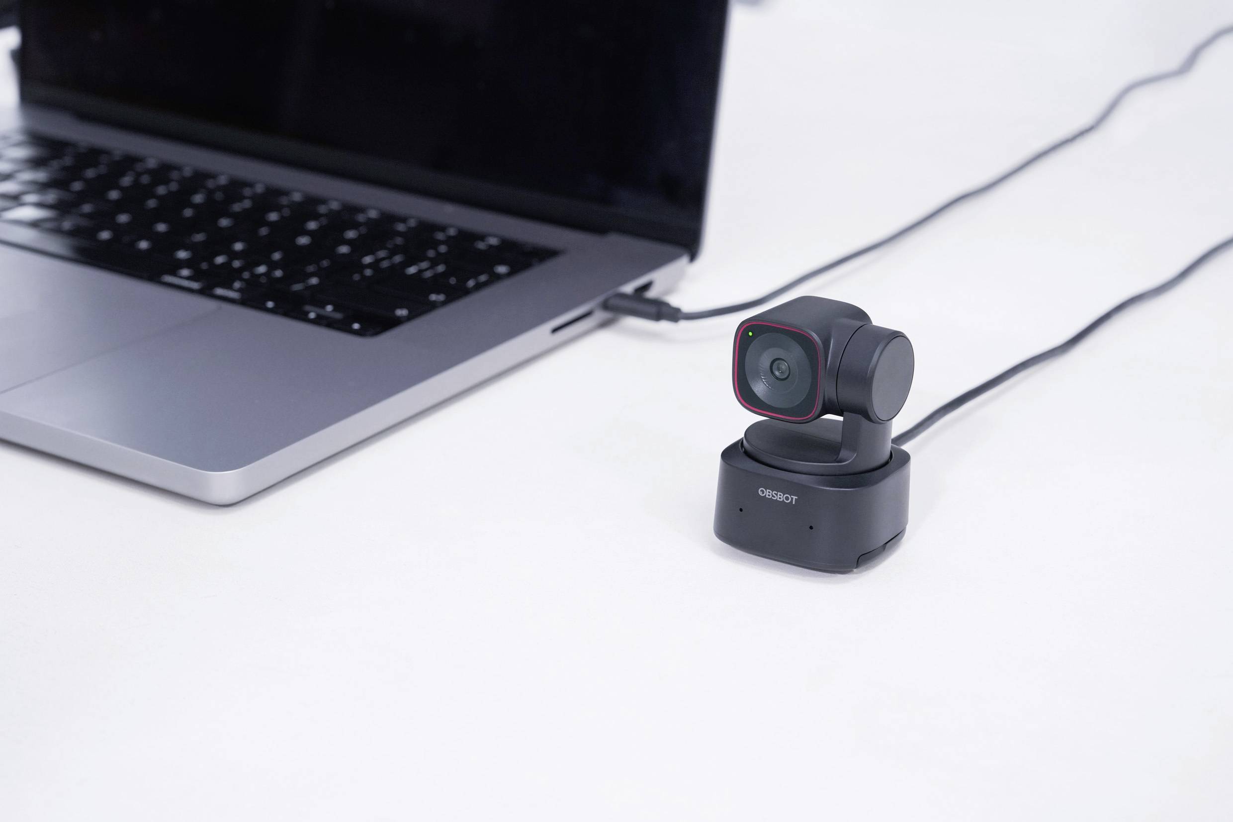 Une webcam connectée est posée à côté d'un ordinateur portable ouvert sur un bureau, prête pour des enregistrements vidéo ou des réunions en ligne.