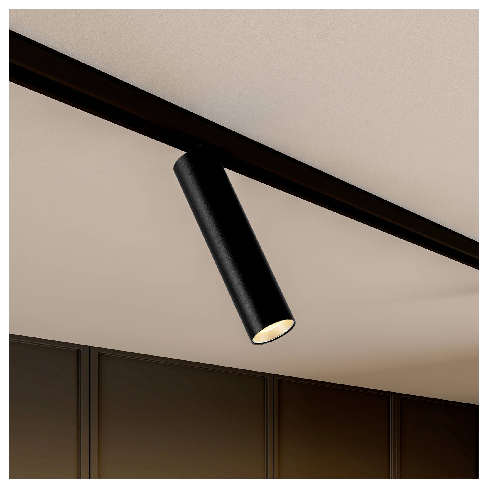 Spot cylindrique noir sur rail de plafond, orienté vers le bas au-dessus de panneaux muraux sombres.