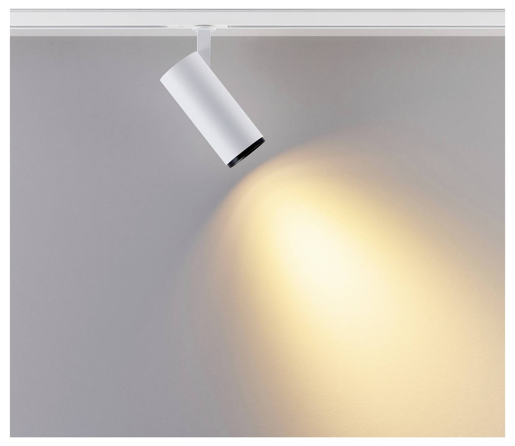 Un spot sur rail blanc fixé au plafond projette une lumière chaude vers le bas sur un mur gris.