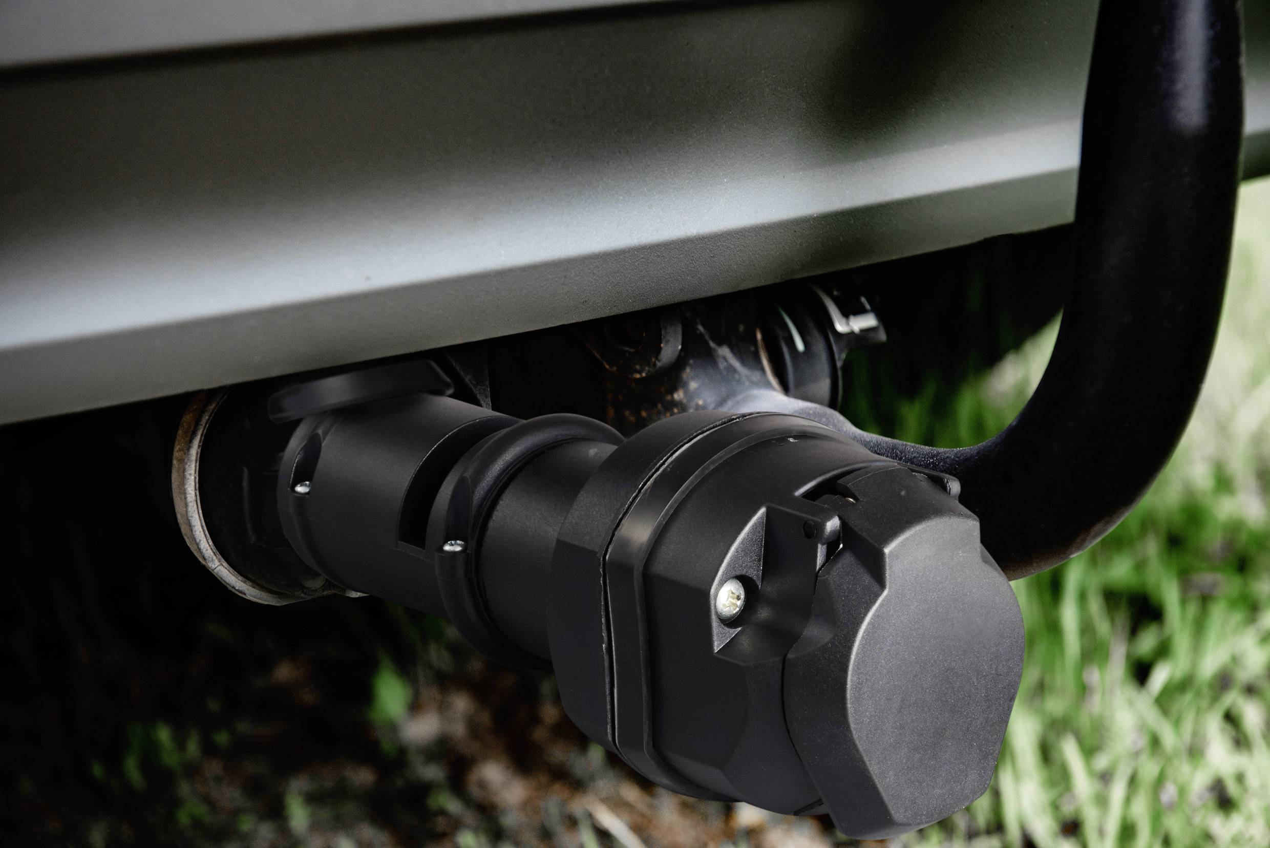 Gros plan sur un verrou d'attelage de remorque sur une voiture, protégeant l'attelage contre le vol. De l'herbe est visible en arrière-plan.