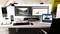 Un poste de travail de bureau avec deux écrans affiche un logiciel de retouche d'image et un tableur. Un ordinateur portable montre un appel vidéo.