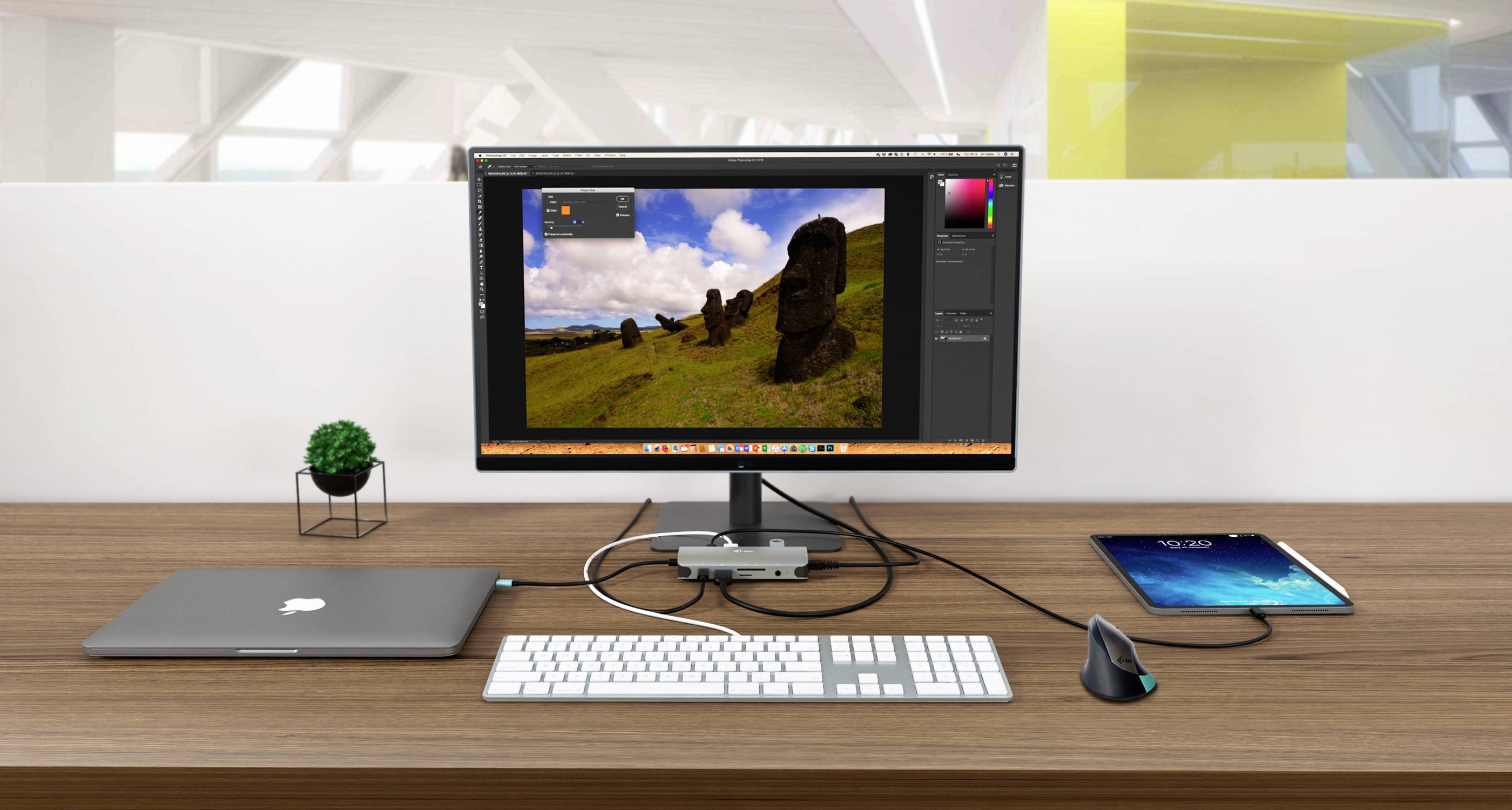 Un bureau avec un moniteur affichant un logiciel de retouche d'image. À côté, un ordinateur portable, un clavier, une souris et une tablette.