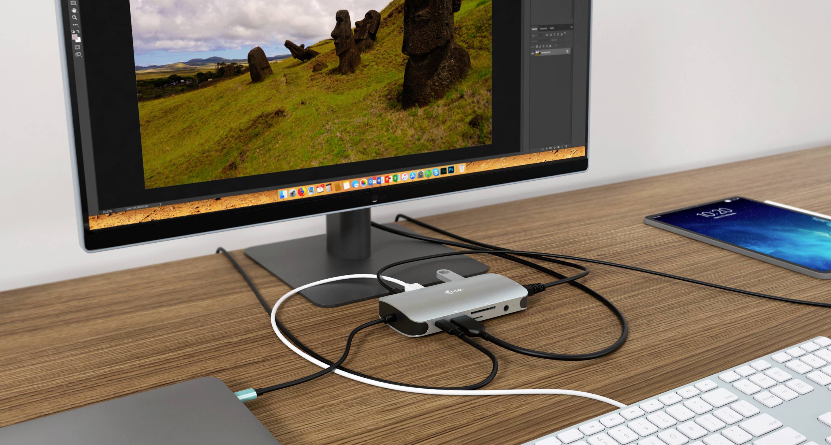 Poste de travail avec un écran d'ordinateur affichant un paysage avec des statues Moaï, connecté à plusieurs câbles via un hub USB.
