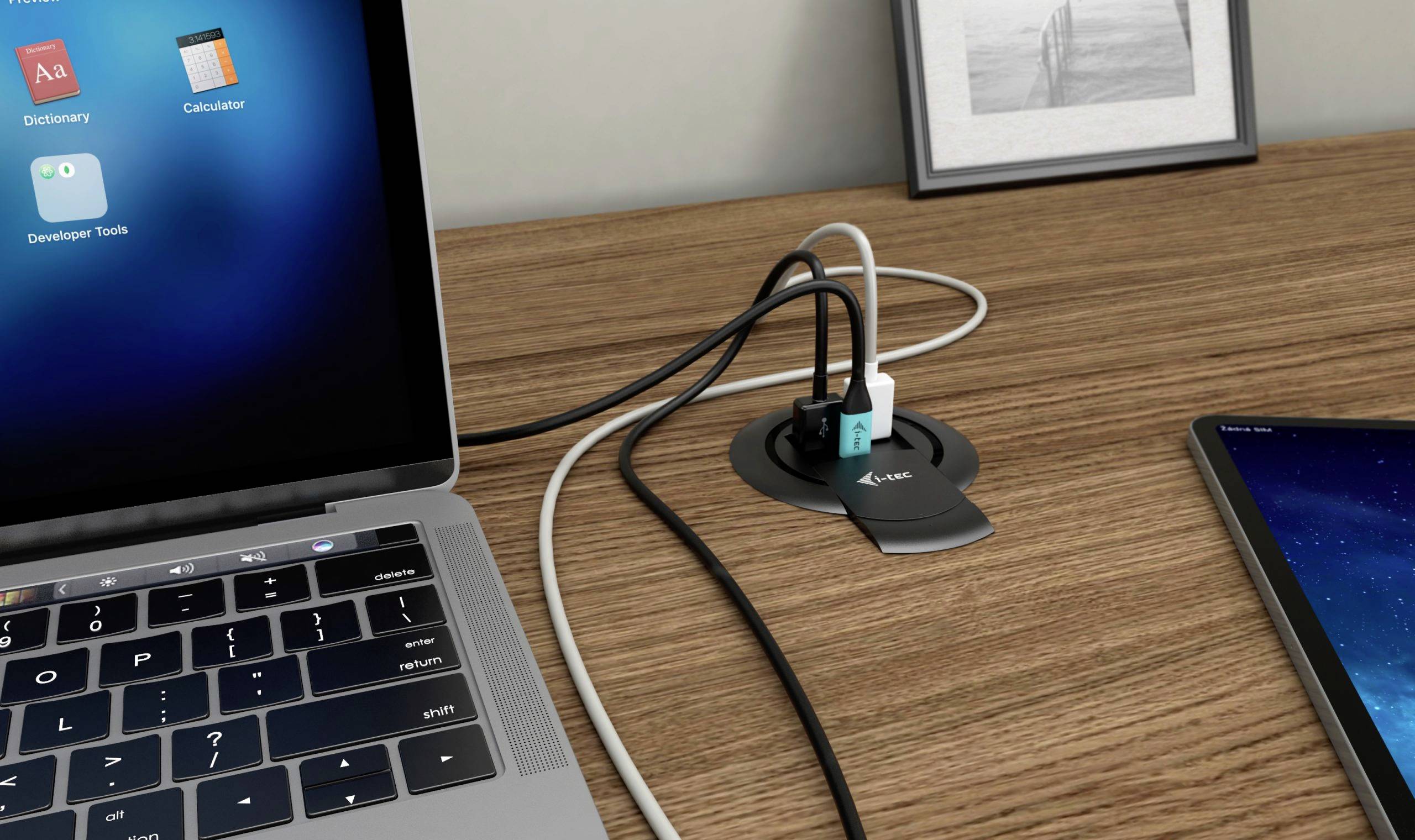 Un ordinateur portable et une tablette sur un bureau, reliés par un support de câbles qui organise les câbles. Image de fond dans un cadre.