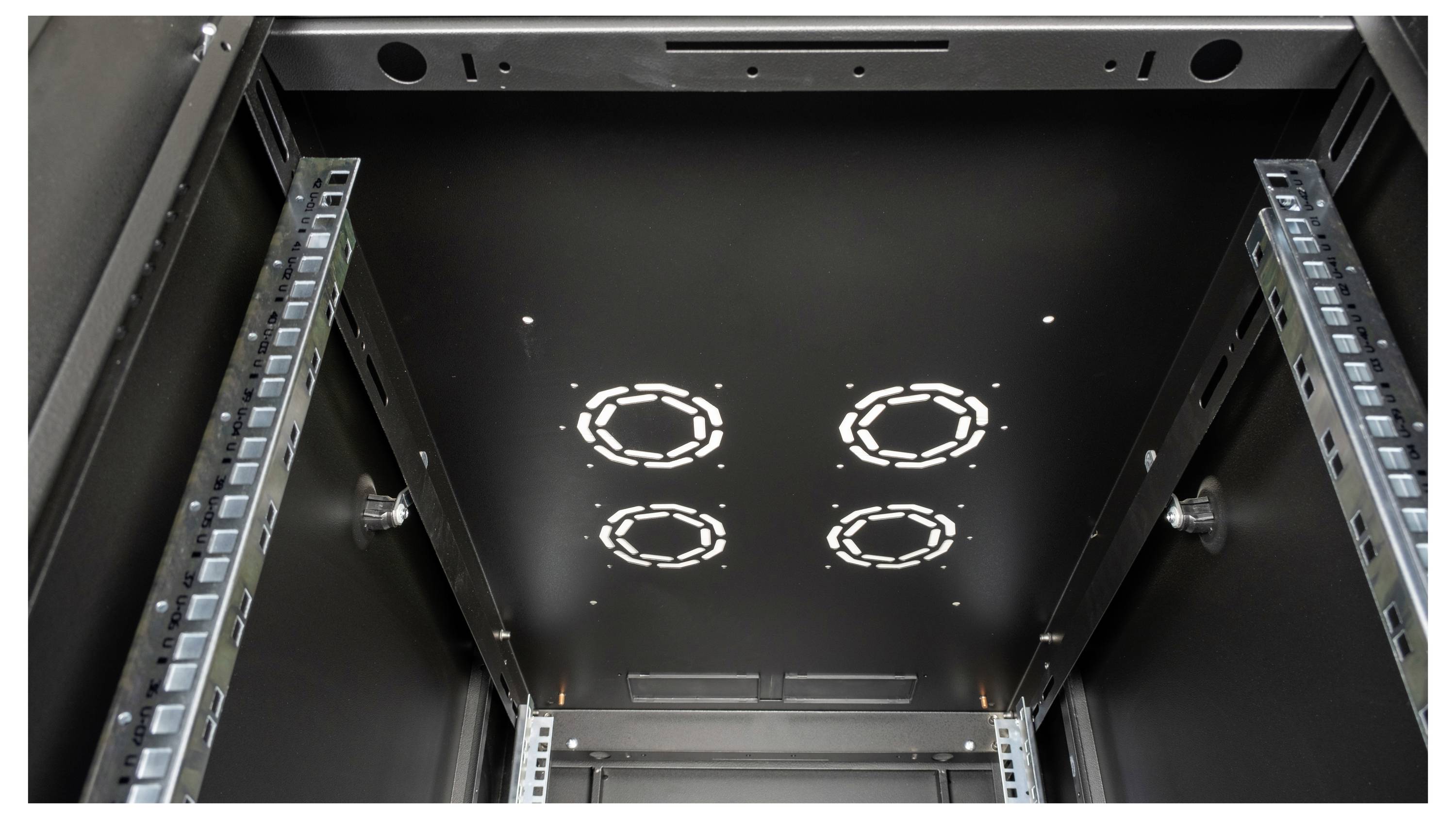 Vue du dessous d'un rack serveur vide. Des rails métalliques et des ouvertures circulaires au plafond pour la gestion des câbles sont visibles.