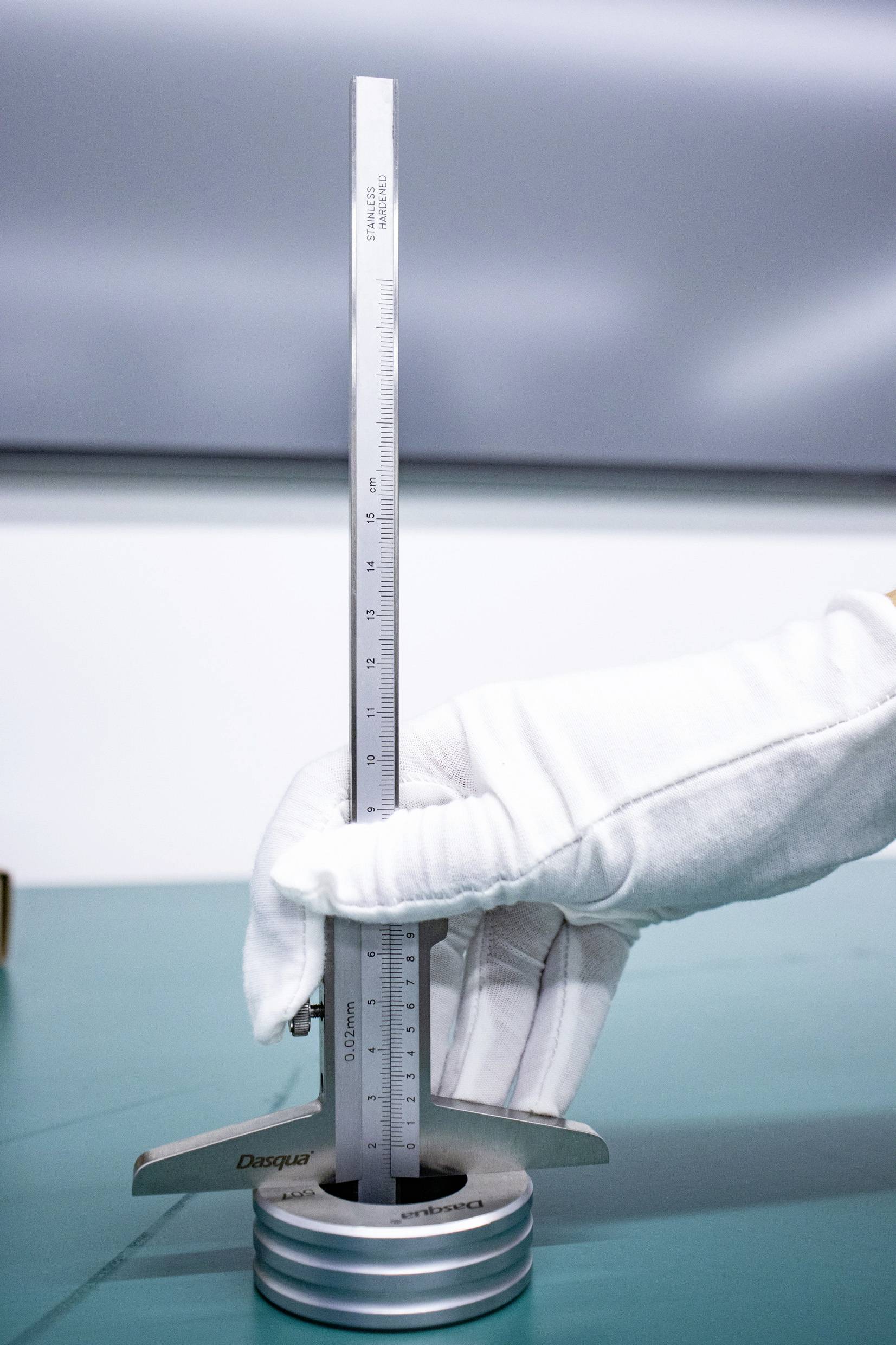 Une main gantée de blanc tient un appareil de mesure vertical posé sur un objet cylindrique placé sur une table.