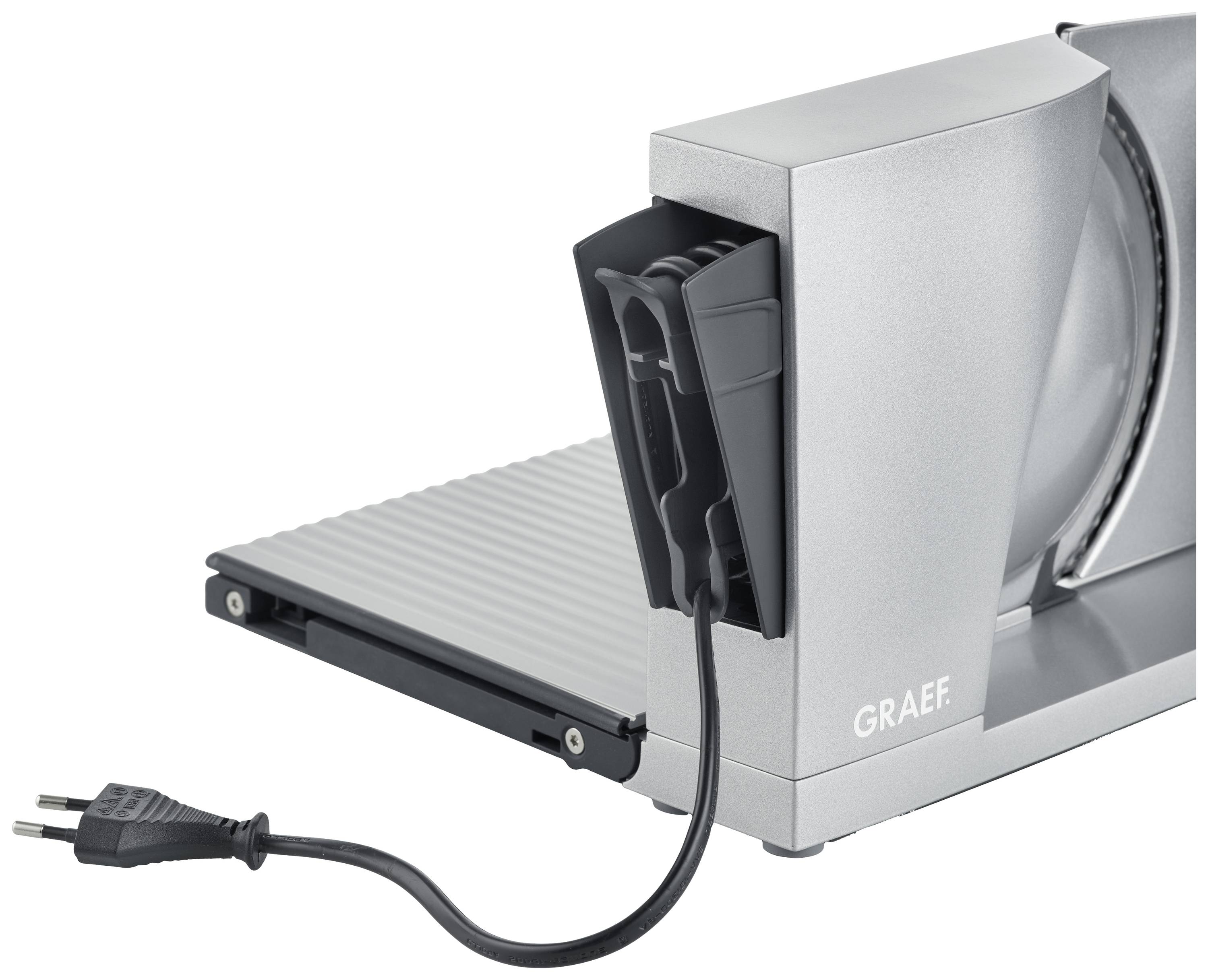 Coupe-tout électrique de couleur argent avec surface de coupe rabattable et fiche secteur européenne, adapté pour couper le pain et les charcuteries.