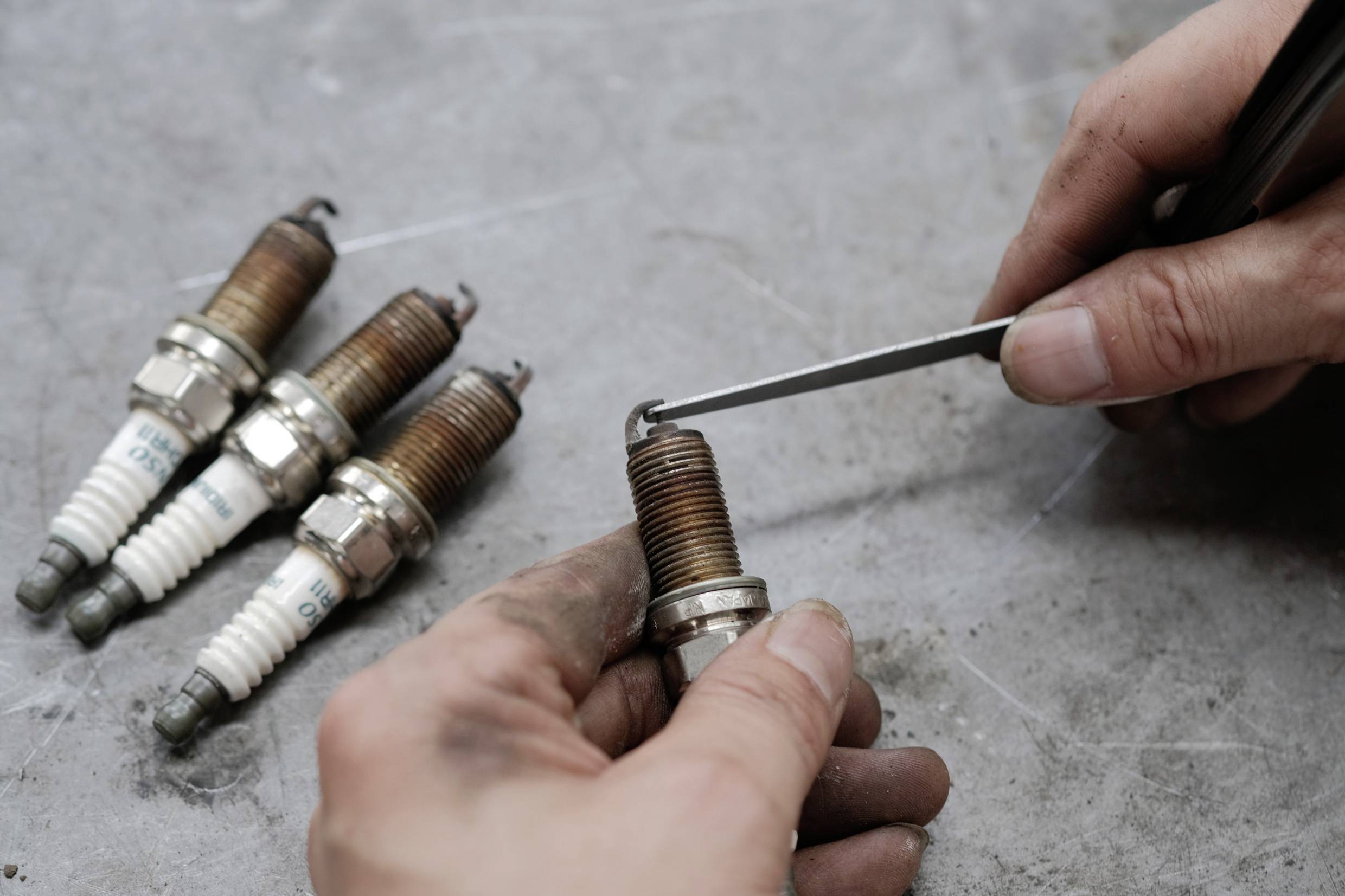 Une personne vérifie des bougies d'allumage avec un tournevis. Quatre autres bougies d'allumage sont posées sur une table d'atelier.
