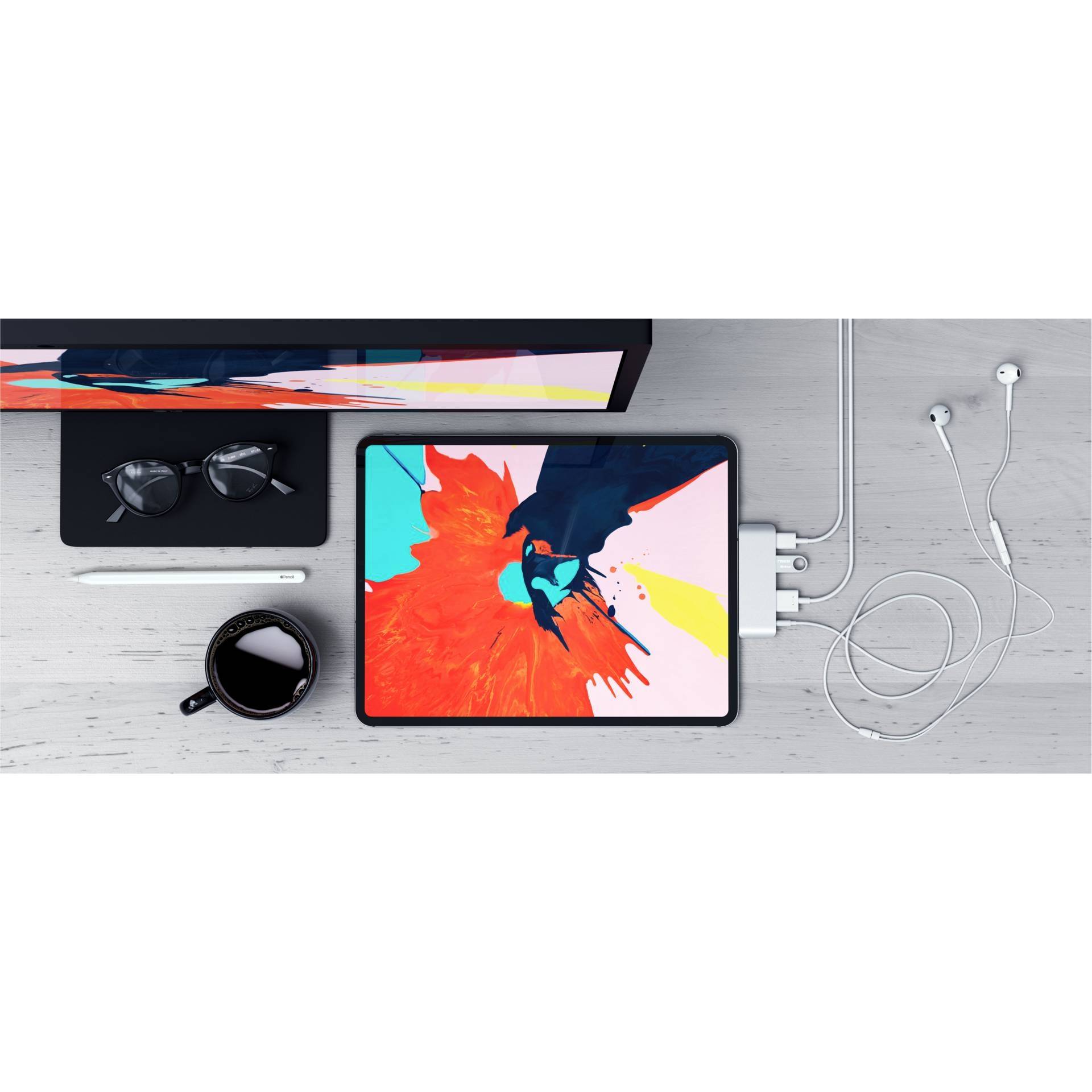 Une tablette sur une table affiche un art coloré. À côté, une tasse de café, des écouteurs et des lunettes. Scène de technologie et de créativité.