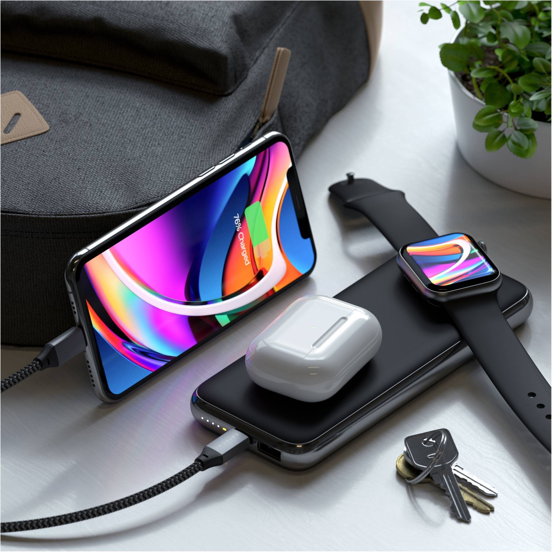 Smartphone, chargeur sans fil, écouteurs et montre connectée sur une table à côté des clés et d'une plante. Appareils en cours de charge.