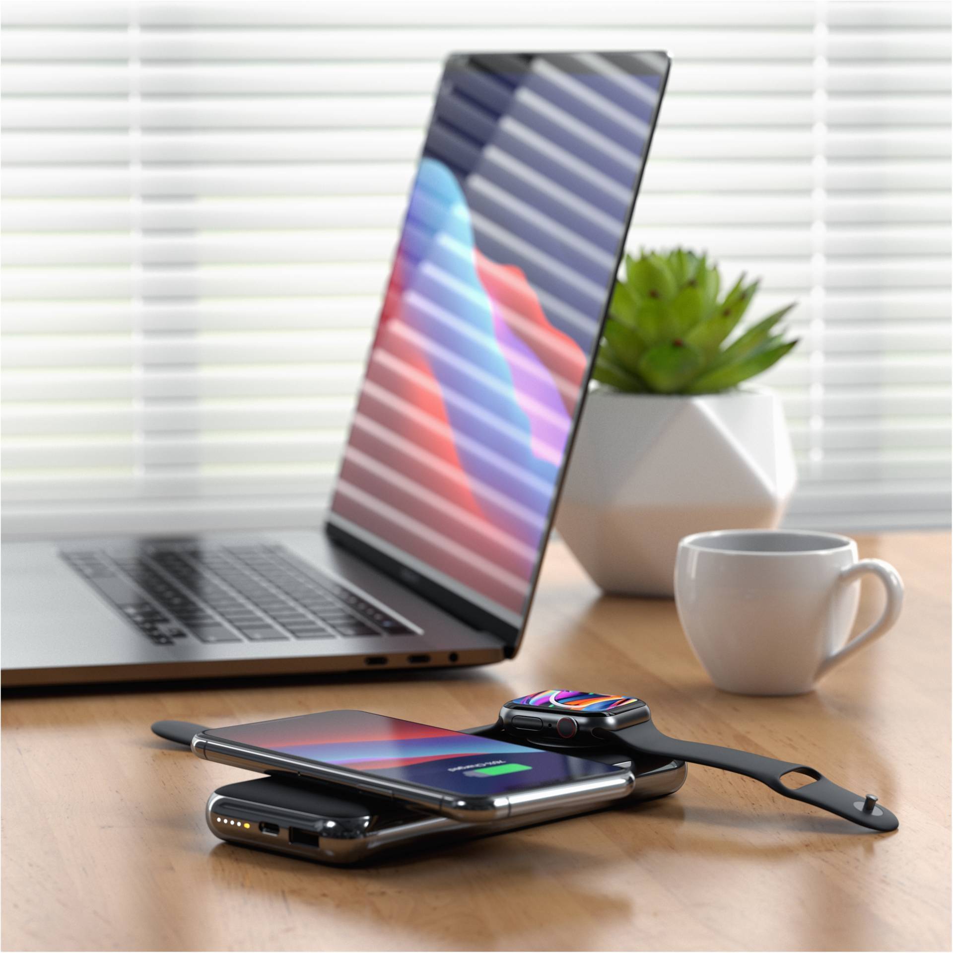 Un ordinateur portable posé sur une table, l'écran allumé. Un smartphone et une montre connectée se chargent sans fil ; une plante et une tasse en arrière-plan.