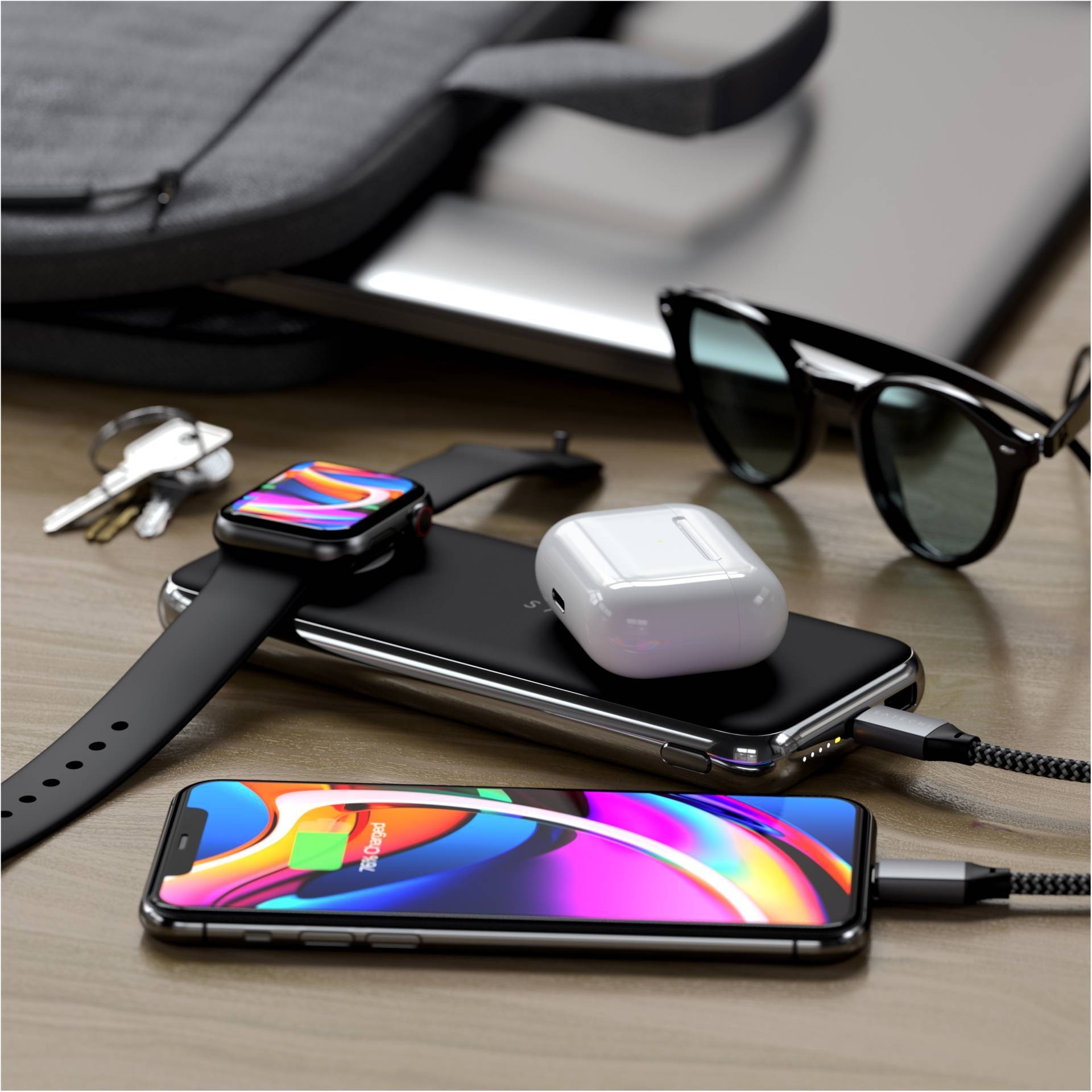 Une table de travail avec un smartphone, une montre connectée, des écouteurs sans fil, des lunettes de soleil et des clés. Tous les appareils sont en cours de chargement.