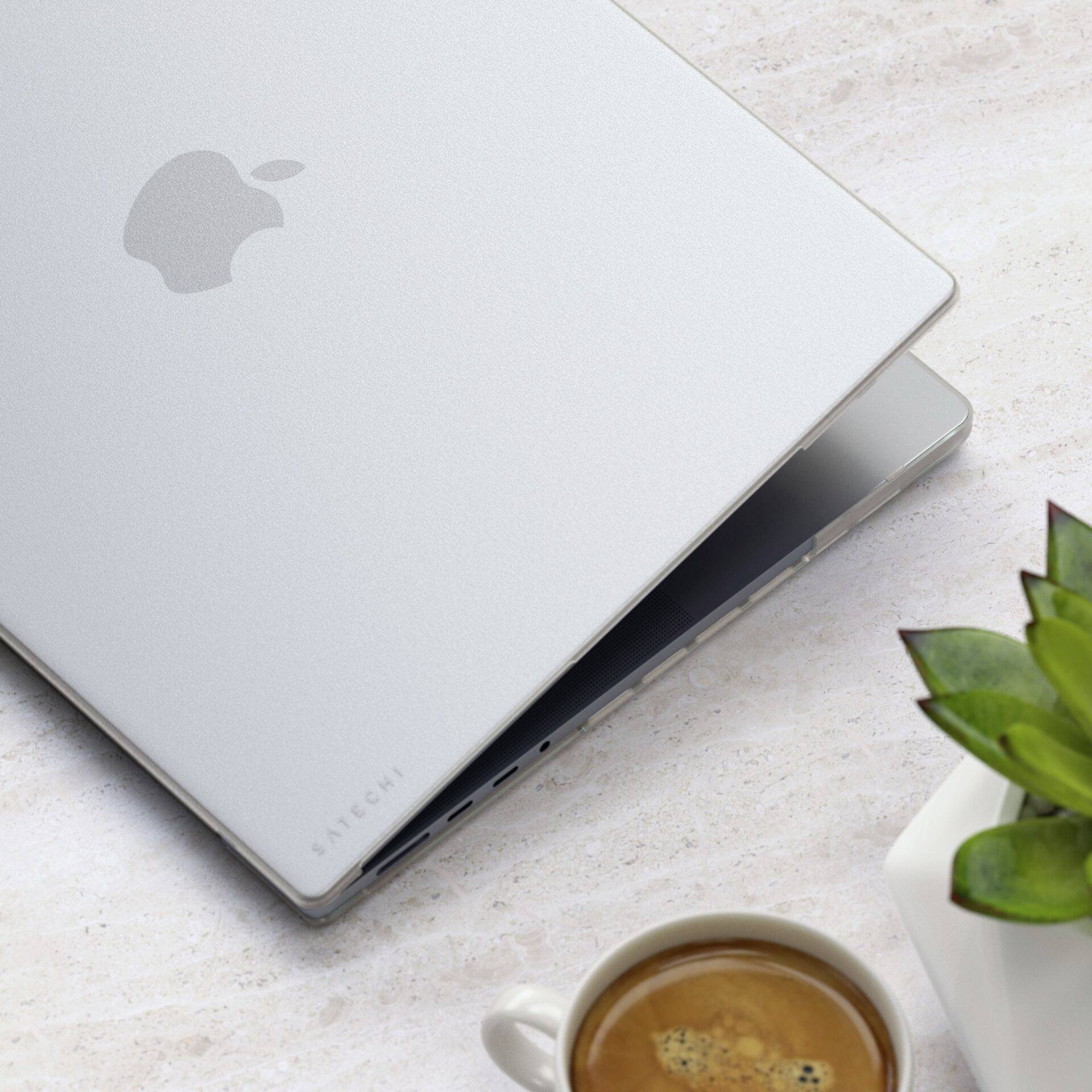Un ordinateur portable argenté est à moitié ouvert sur un bureau, à côté d'une tasse de café et d'une petite plante.