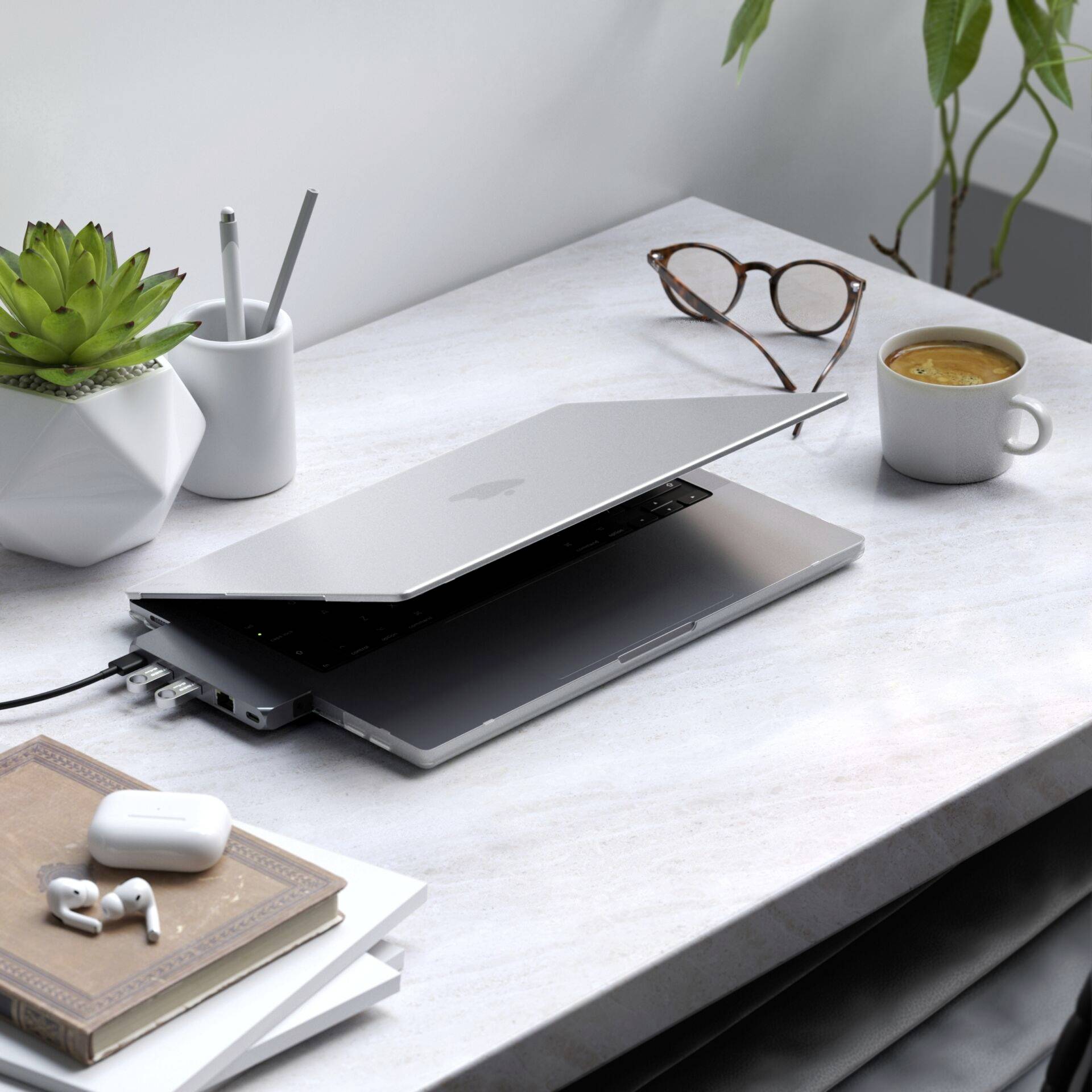 Un ordinateur portable à moitié ouvert sur une table, avec des lunettes, une tasse à café, des plantes et des écouteurs. Un environnement de travail moderne et bien éclairé.
