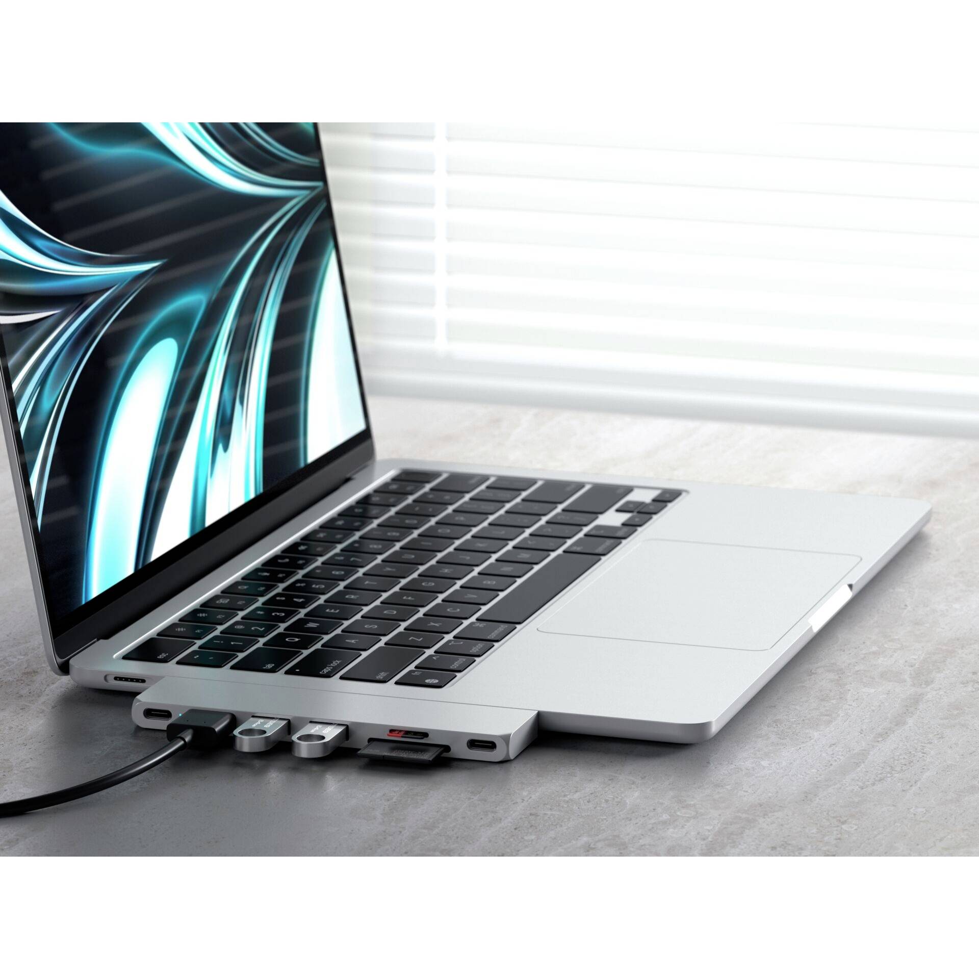 Un ordinateur portable sur une table avec un hub USB connecté et plusieurs câbles. L'écran affiche un motif bleu abstrait.