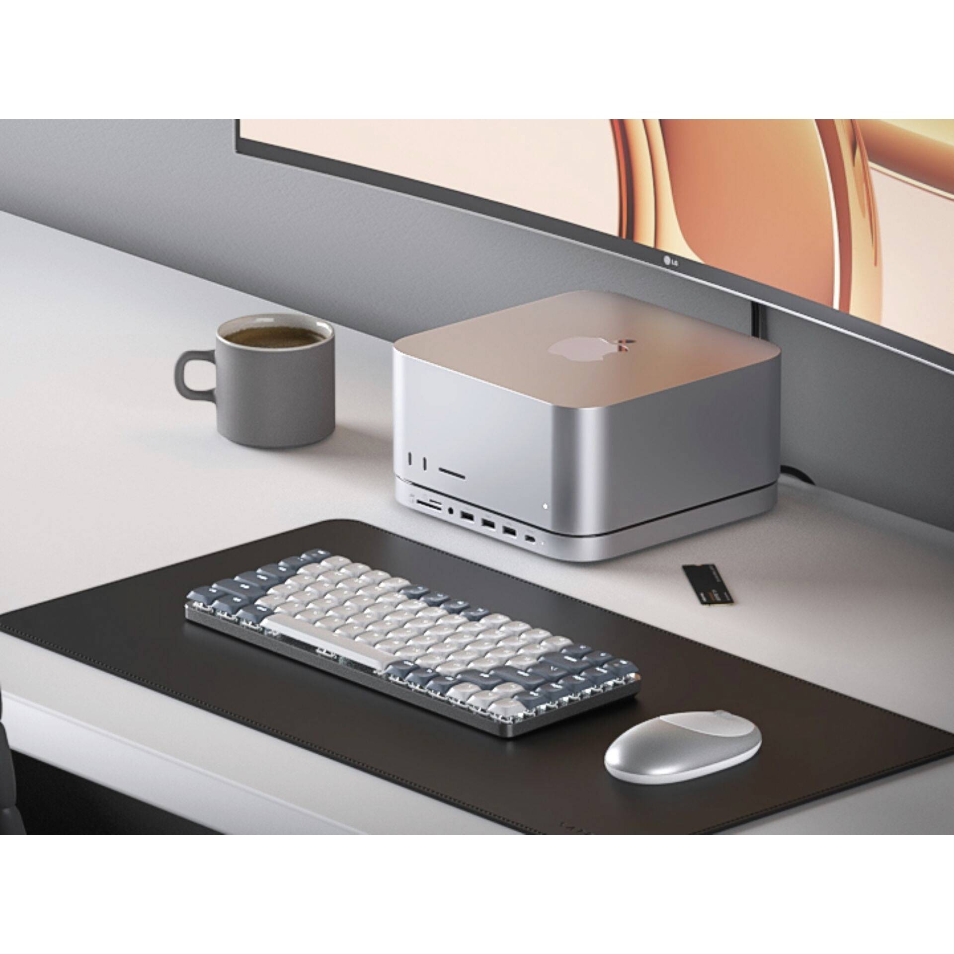 Un bureau moderne avec un moniteur, un Mac Mini, un clavier externe, une souris, une clé USB et une tasse de café sur un tapis de souris.