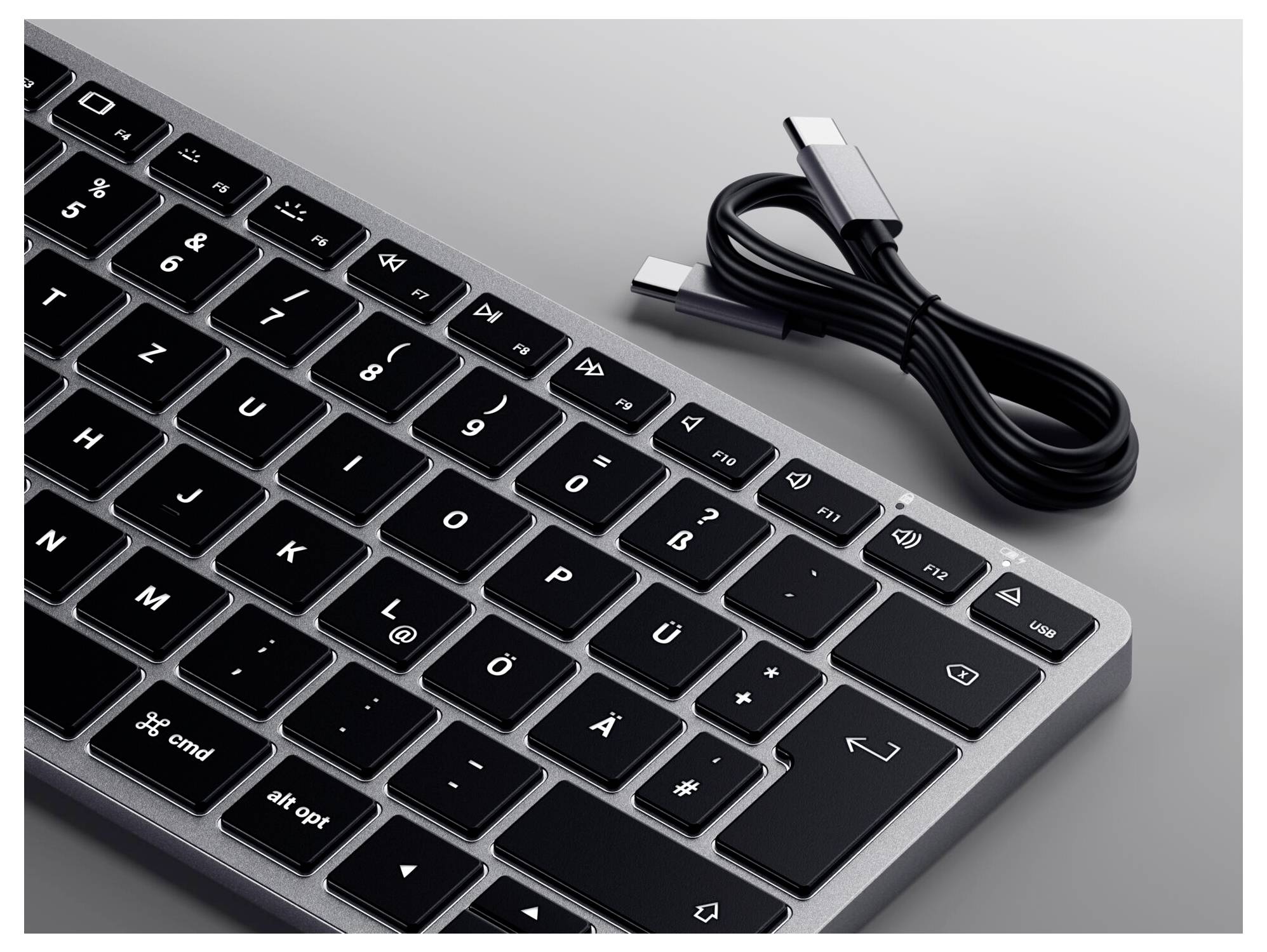 Clavier sans fil avec touches noires et cadre argenté, à côté d'un câble USB-C.