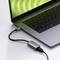 Un ordinateur portable gris argenté avec un écran vert est connecté à un adaptateur USB-C via un câble noir.