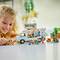 Un enfant joue avec un modèle de camping-car construit en blocs de construction, entouré de petites figurines et d'arbres sur une table.