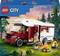 Ensemble Lego avec un camping-car rouge, deux personnages assis autour d'un feu de camp dans la forêt. Texte : '6+ City Camping-car de vacances 385 pcs'.