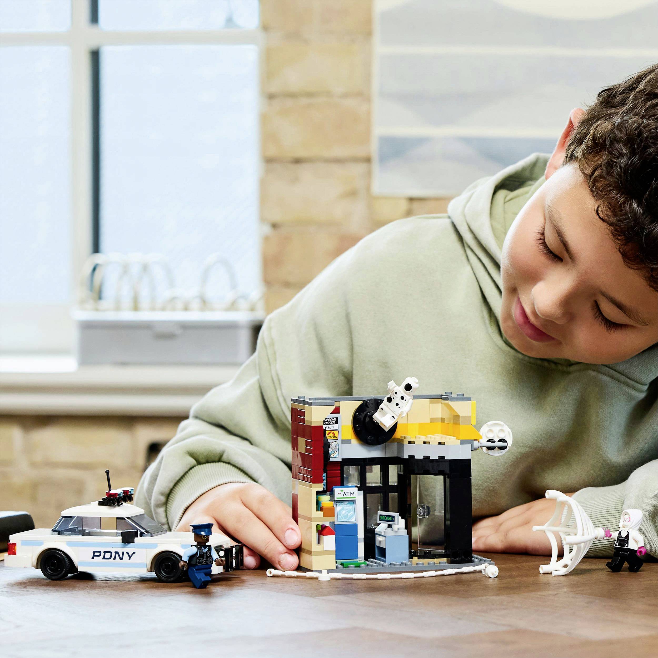 Un enfant joue concentré avec des blocs de construction sur une table, avec un véhicule de police à proximité. Une fenêtre est visible en arrière-plan.