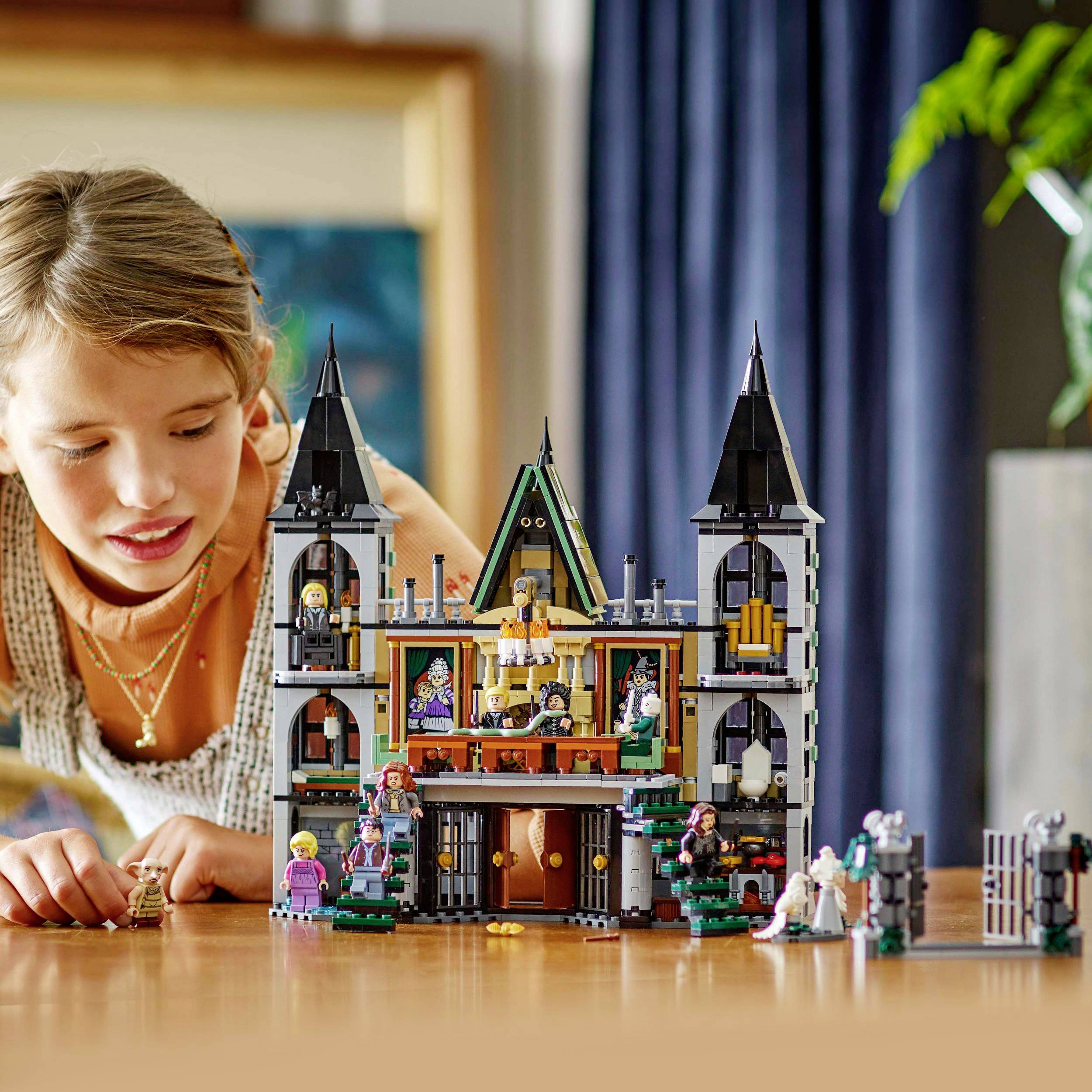 Un enfant joue avec un ensemble LEGO représentant une maison hantée. L'ensemble présente des figurines et des détails effrayants sur une table en bois.