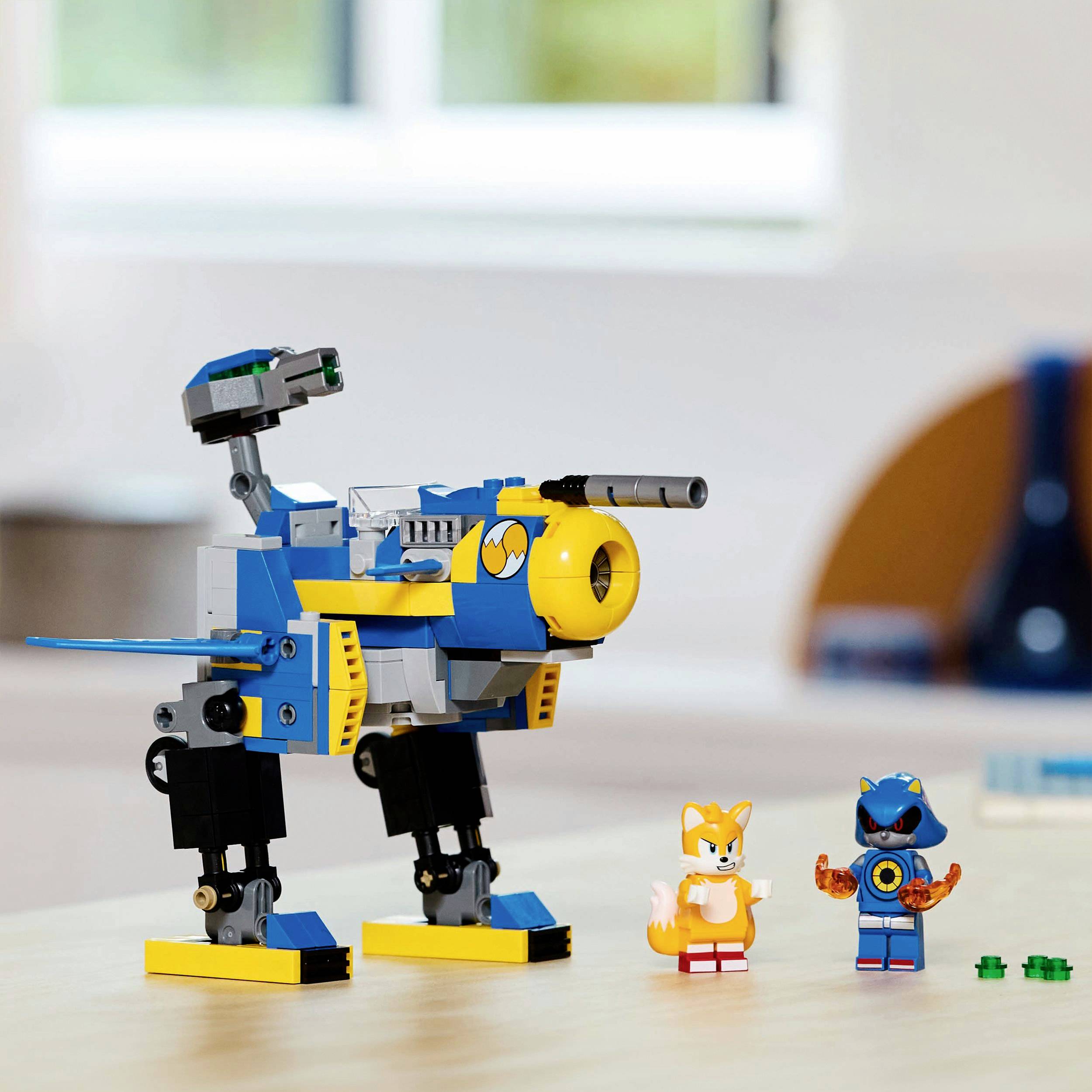 Un jouet de construction bleu et jaune avec des jambes mobiles et deux petites figurines est posé sur une table dans une pièce lumineuse.