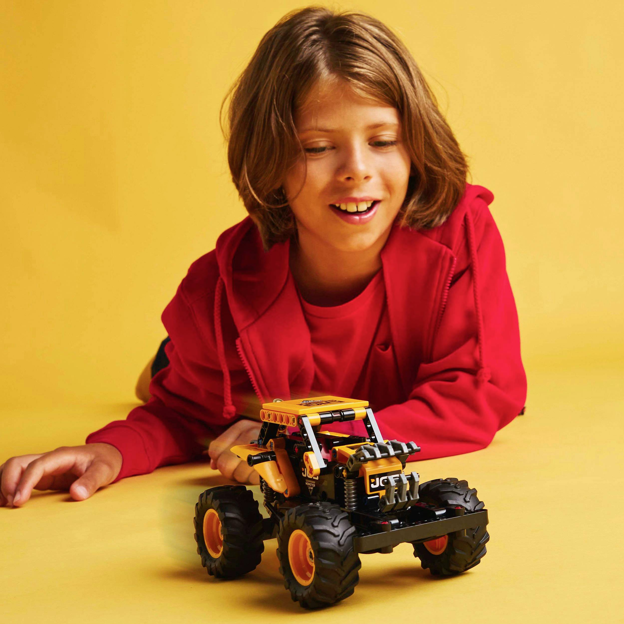 Un enfant vêtu de rouge joue joyeusement avec un monster truck miniature sur un fond jaune.