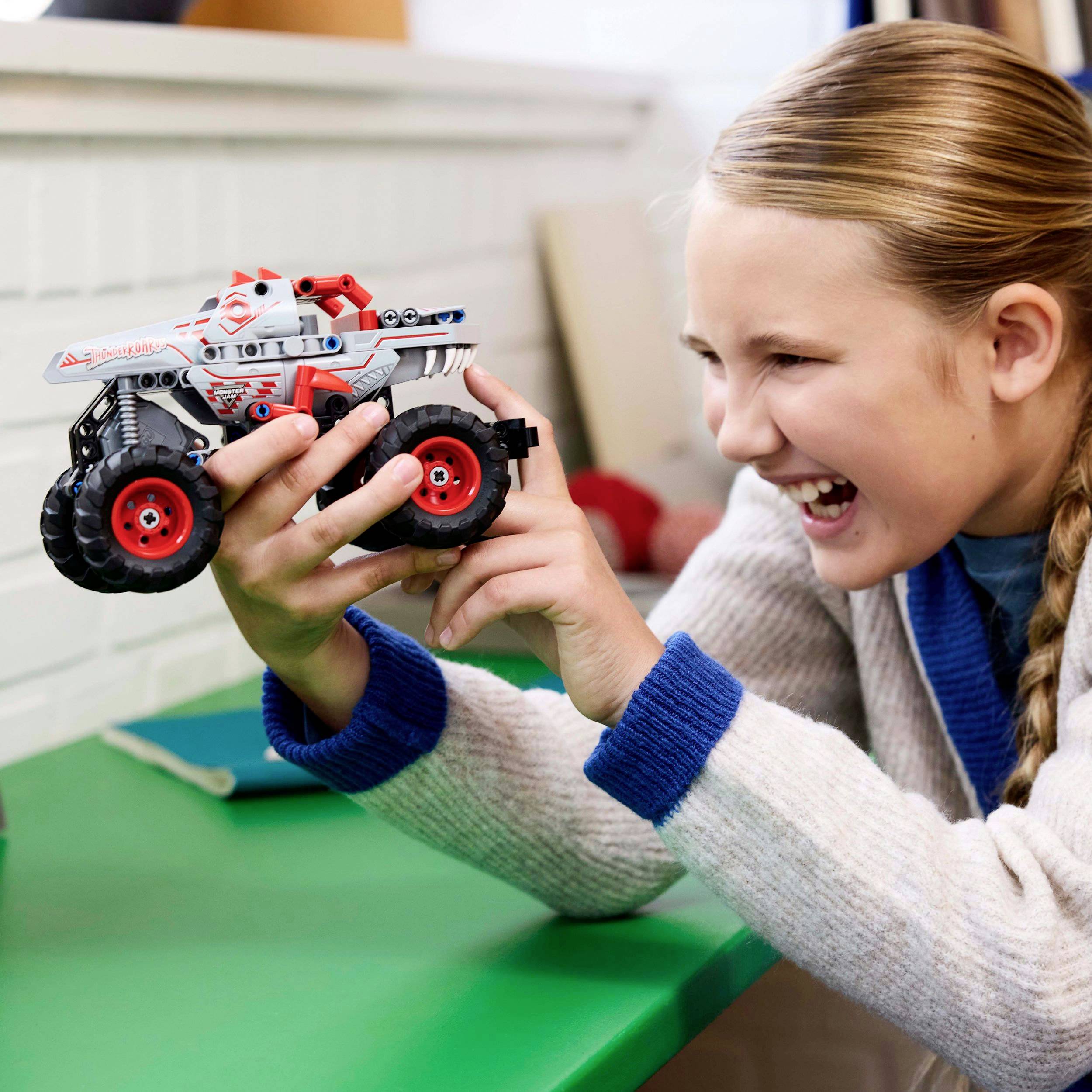Un enfant aux cheveux blonds joue avec enthousiasme avec une voiture télécommandée sur une table.