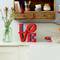 Une étagère de cuisine avec de la vaisselle. Sur le plan de travail, il y a un vase en verre avec des fleurs et les lettres 'LOVE' en rouge à côté d'un bol rouge.