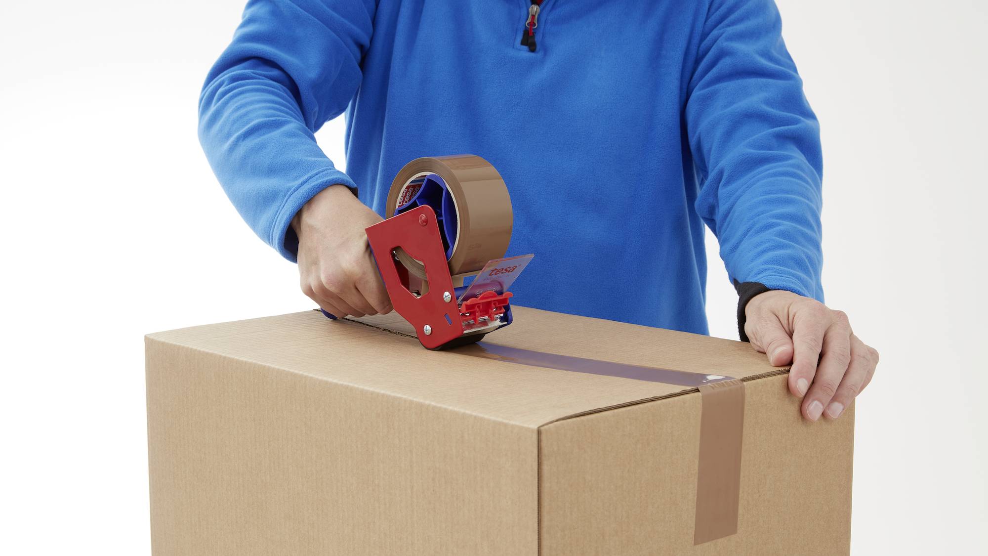 Une personne portant un pull bleu scelle un carton avec du ruban adhésif.