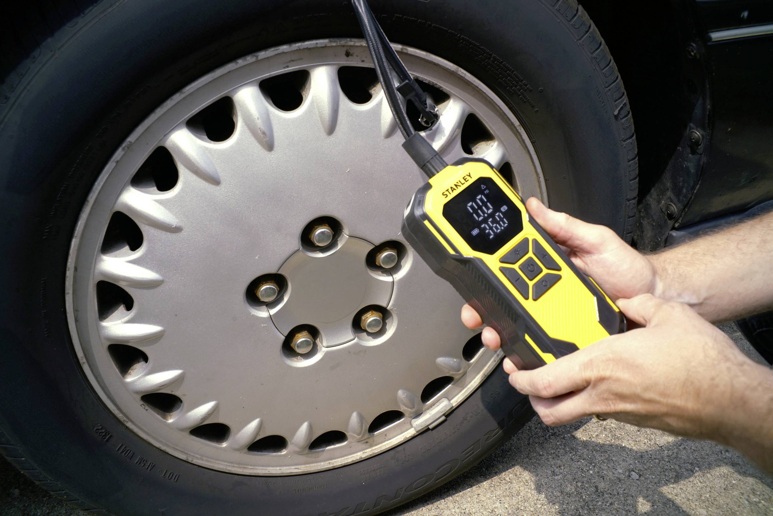 Une personne mesure la pression d'un pneu de voiture à l'aide d'un manomètre numérique. L'appareil affiche '0.0' et '3.0C'.