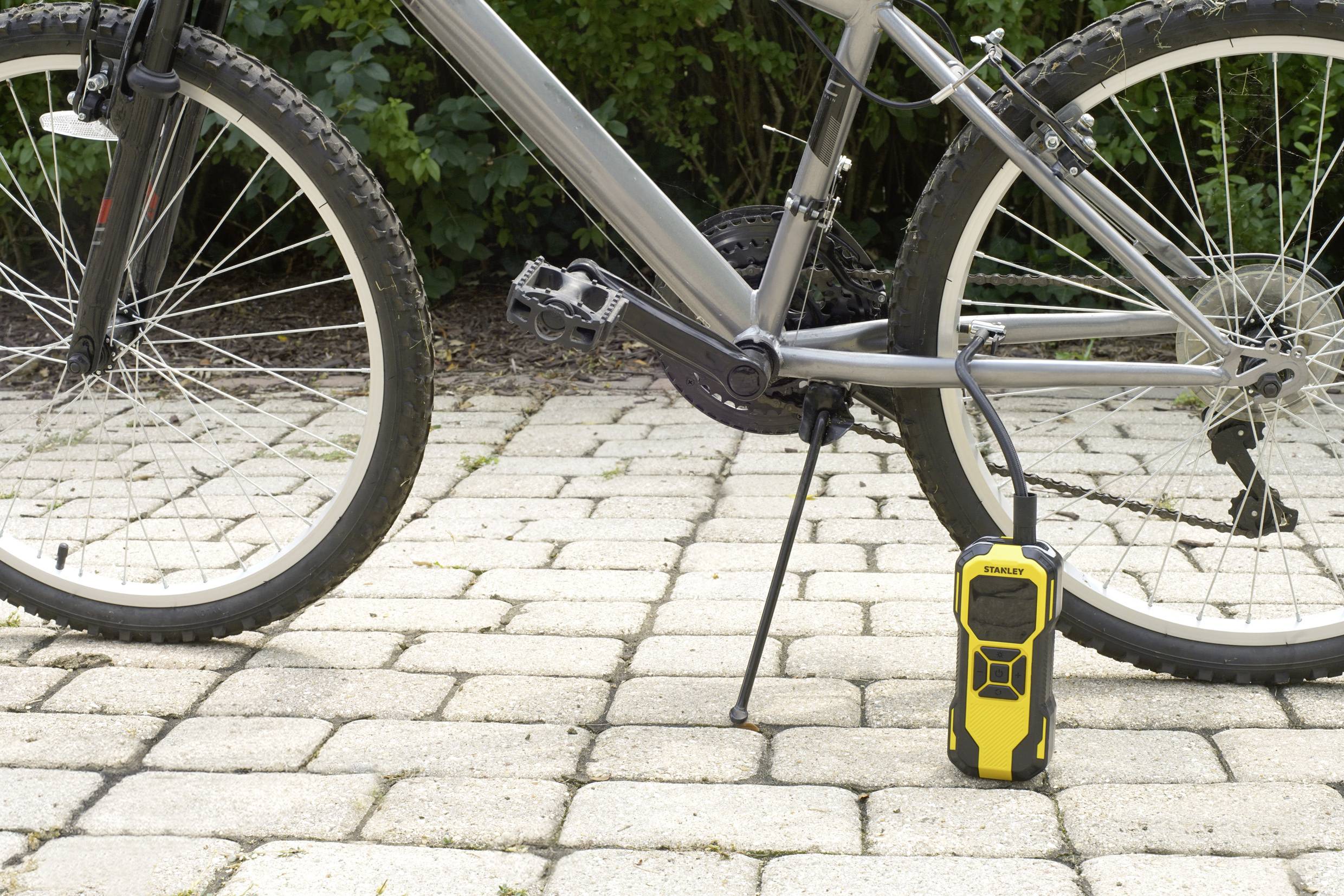 Un vélo noir sur des pavés se trouve à côté d'une pompe à vélo portable jaune. Le vélo est immobile et la pompe est prête à l'emploi.
