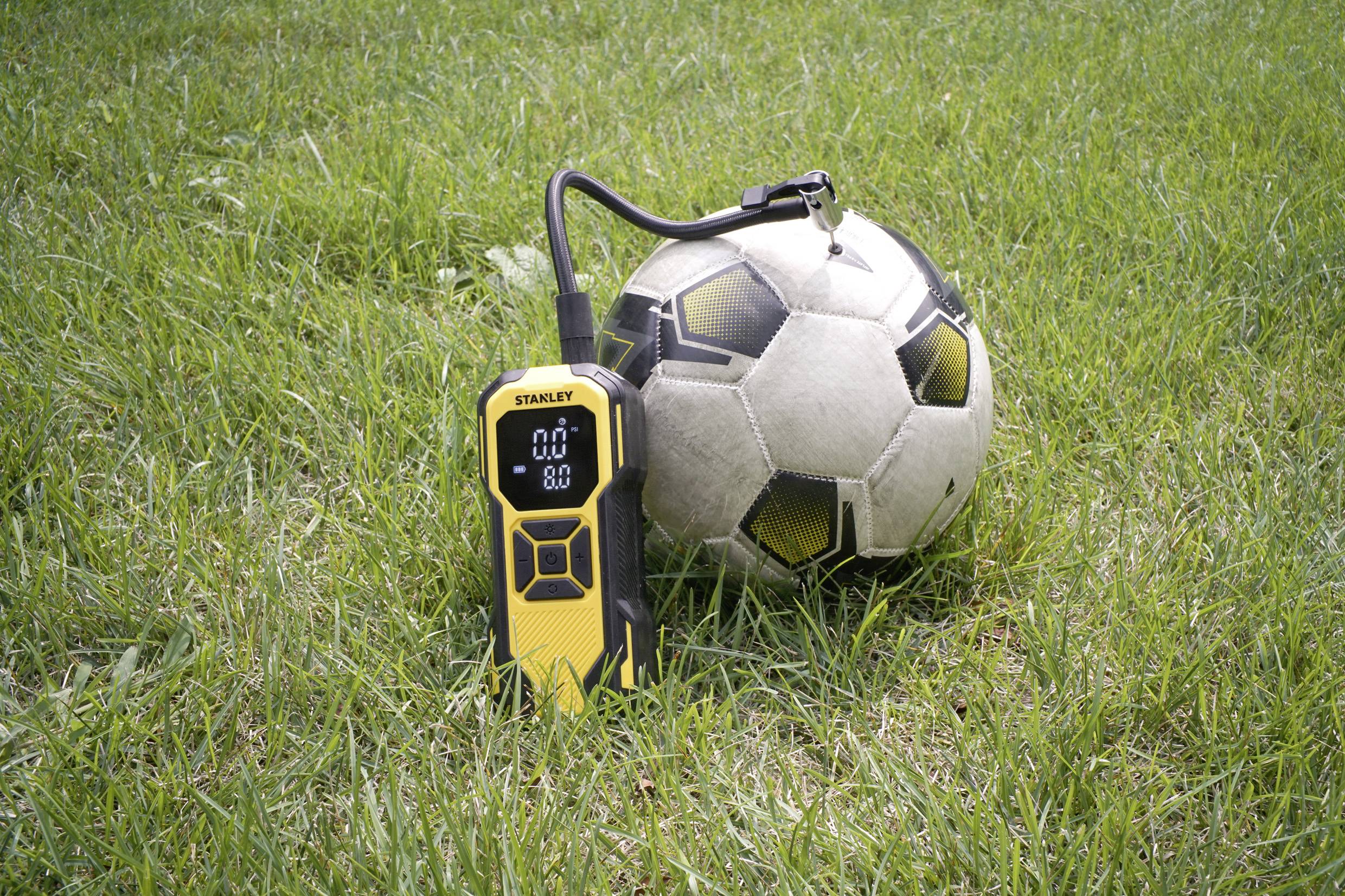 Un ballon de football est posé sur l'herbe à côté d'un manomètre numérique jaune qui affiche une pression de 0,0.