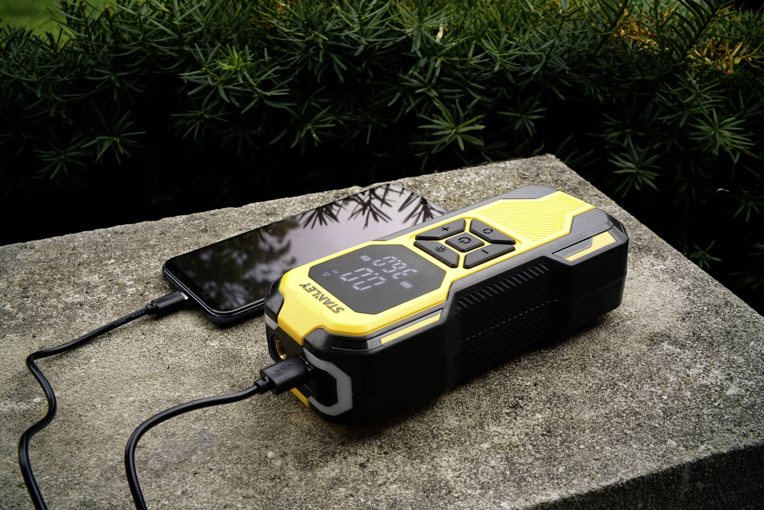 Appareil de démarrage SCHWAIGER 300A : Un appareil de démarrage portable jaune et noir charge un smartphone. Une plante verte est visible en arrière-plan.
