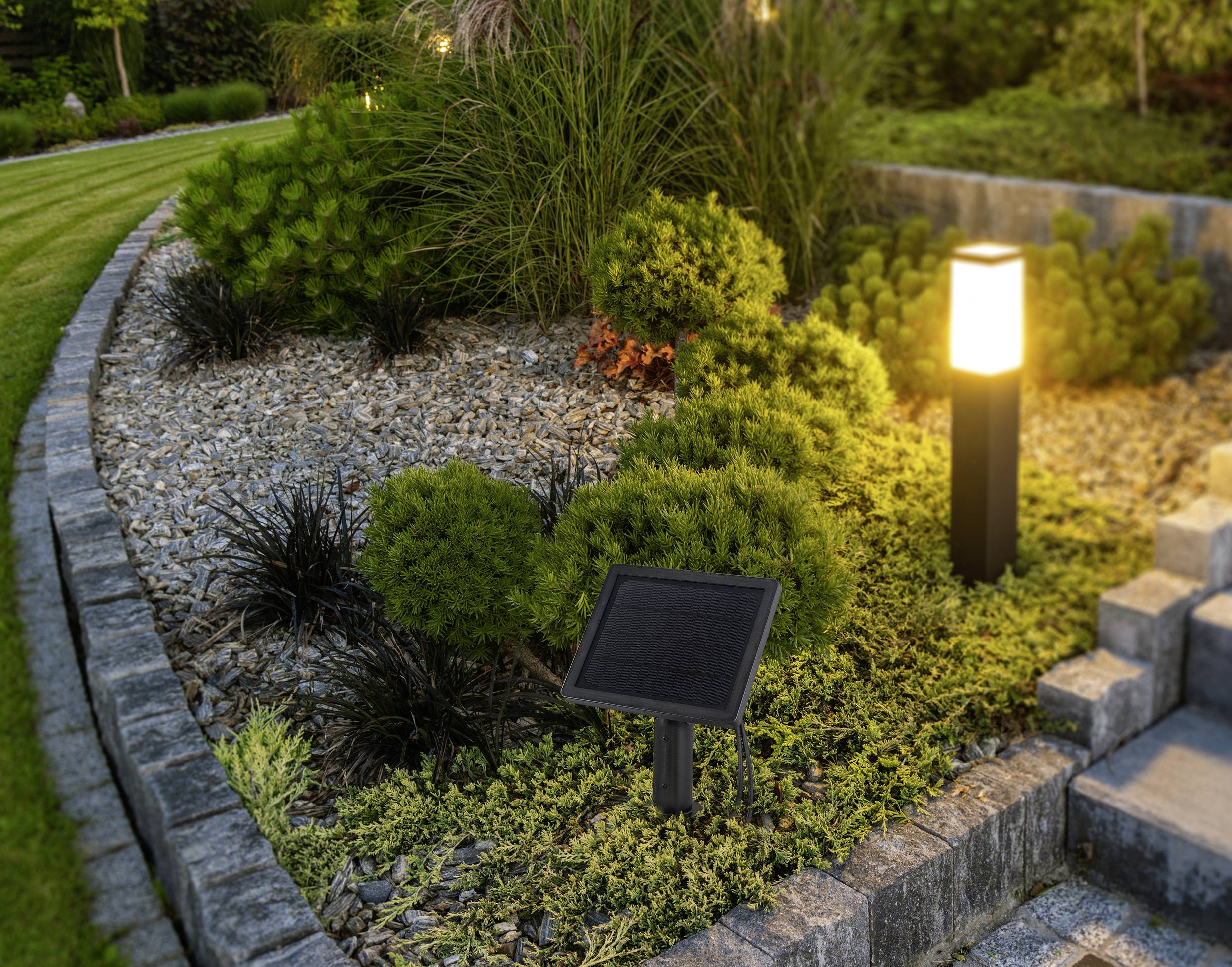 Un jardin paysager avec un panneau solaire près d'un luminaire extérieur illuminé, entouré d'arbustes et de marches en pierre menant à une terrasse.
