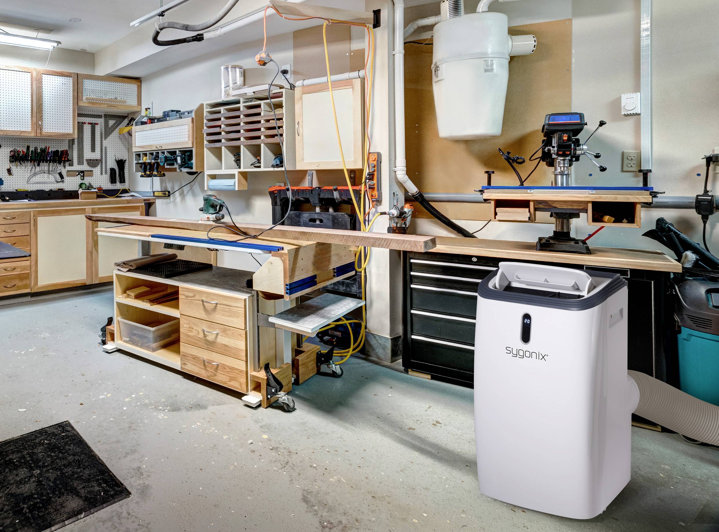 Dans un atelier bien équipé, un déshumidificateur blanc est installé. À l'arrière-plan, on peut voir des outils et un établi.