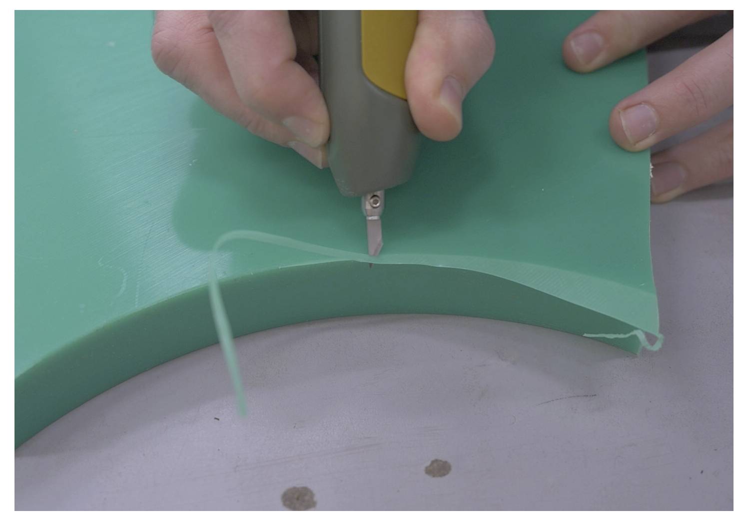 Un gros plan de mains utilisant un cutter rotatif pour sculpter une pièce de mousse verte incurvée, démontrant précision et savoir-faire artisanal.