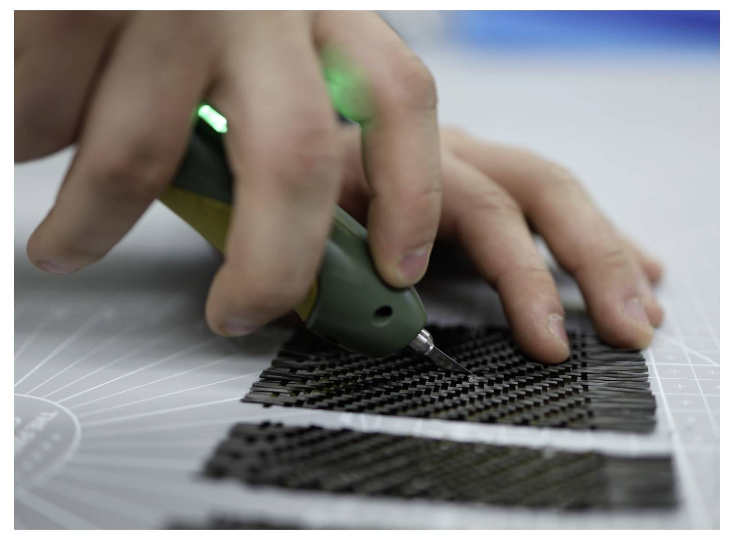 Une personne utilise un outil portatif pour travailler avec précision sur de petits matériaux noirs à motifs, posés sur une surface quadrillée, suggérant un artisanat minutieux.
