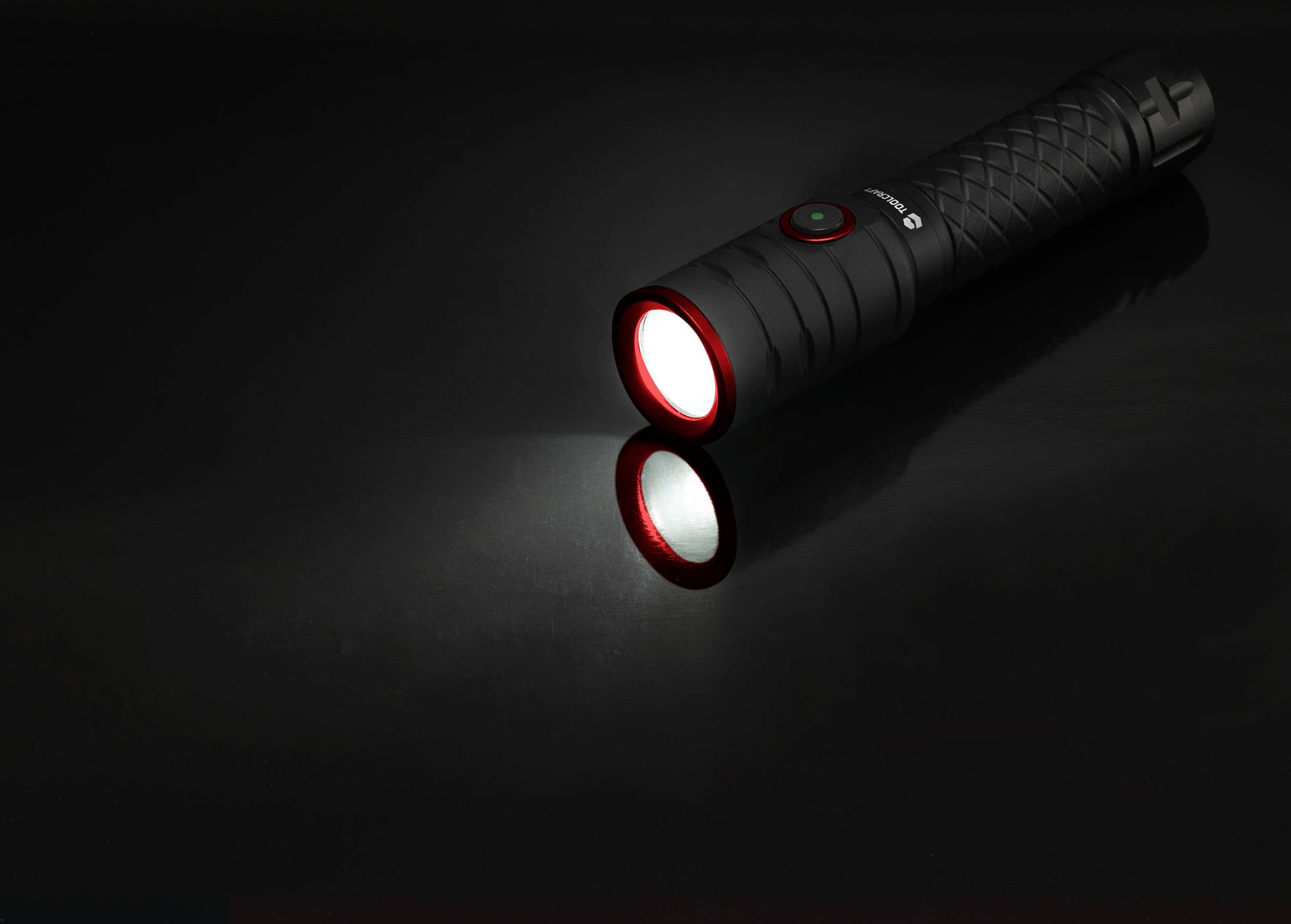 Une lampe de poche noire, posée sur une surface brillante, projette un faisceau blanc vers l'avant.